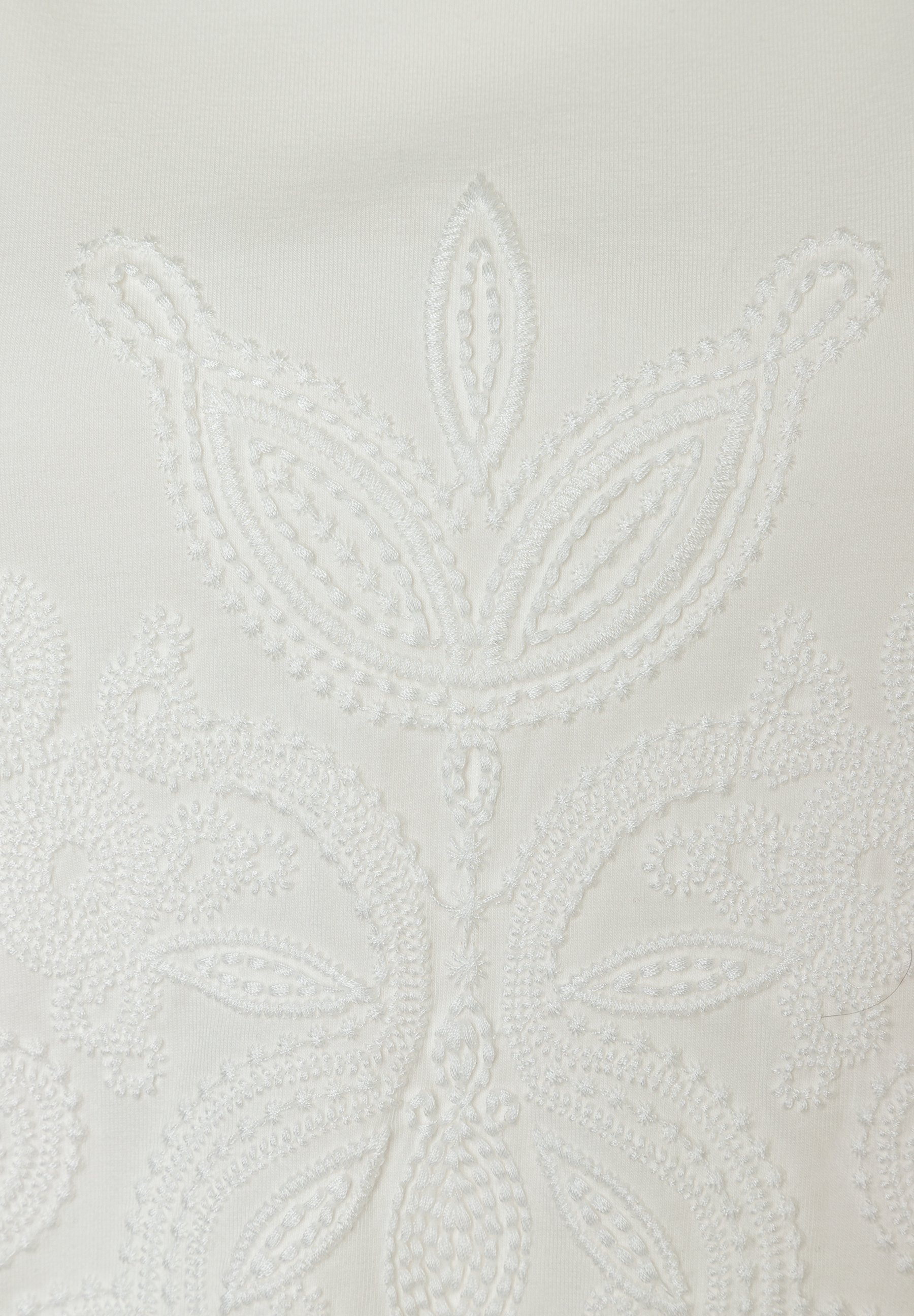 Nahaufnahme eines weißen MORE & MORE Oberteils mit Jersey-Stickerei.