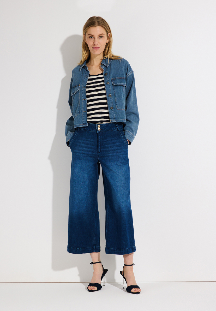 Eine Frau in MORE & MORE Denim-Jeans, pinker Strickjacke und silbernen Schuhen. Eine Frau in MORE & MORE Denim-Jeans, pinker Strickjacke und silbernen Schuhen.