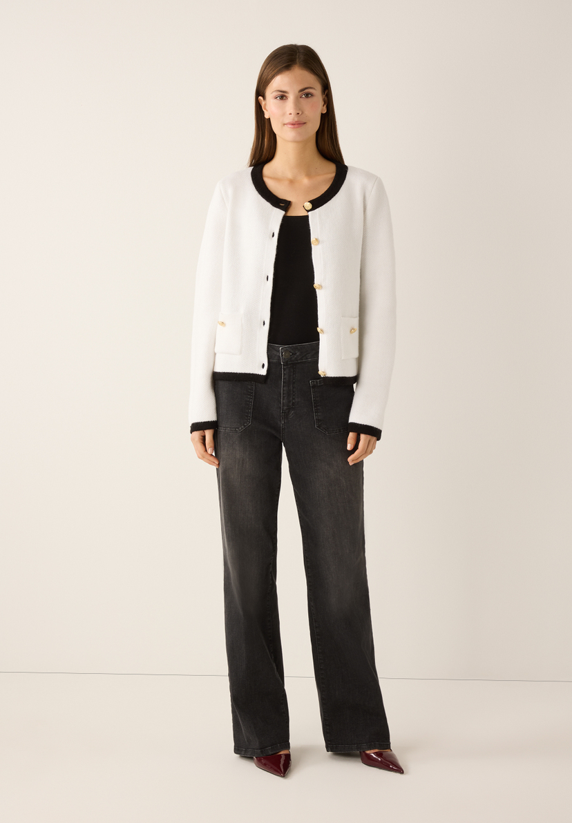 Eine Frau in MORE & MORE Strickware, schwarzem Top und Jeans posiert vor einem hellen Hintergrund. Eine Frau in MORE & MORE Strickware, schwarzem Top und Jeans posiert vor einem hellen Hintergrund.