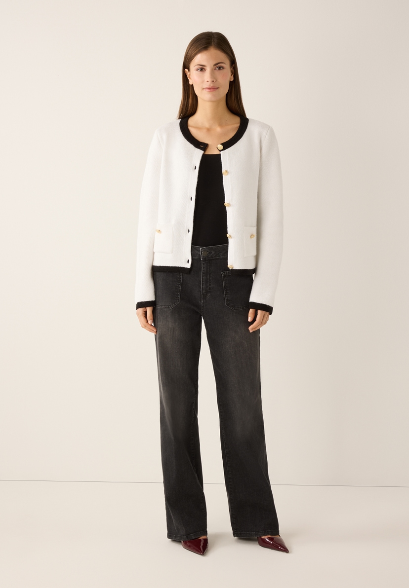 Eine Frau in MORE & MORE Strickware, schwarzem Top und Jeans posiert vor einem hellen Hintergrund. Eine Frau in MORE & MORE Strickware, schwarzem Top und Jeans posiert vor einem hellen Hintergrund.