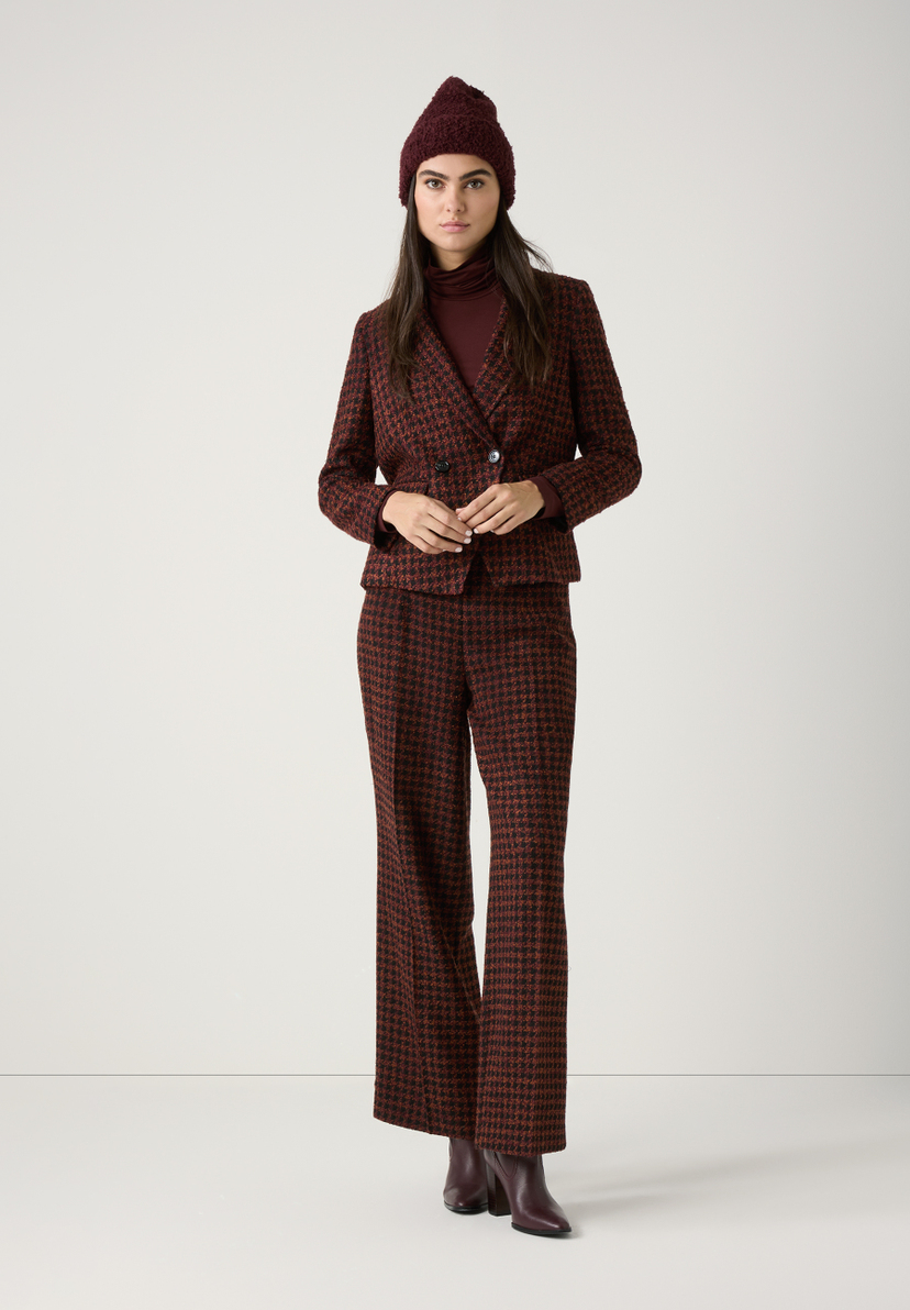 Eine Frau in einem Hosenanzug von MORE & MORE aus Bouclé mit passender Mütze und Rollkragenpullover. Eine Frau in einem Hosenanzug von MORE & MORE aus Bouclé mit passender Mütze und Rollkragenpullover.