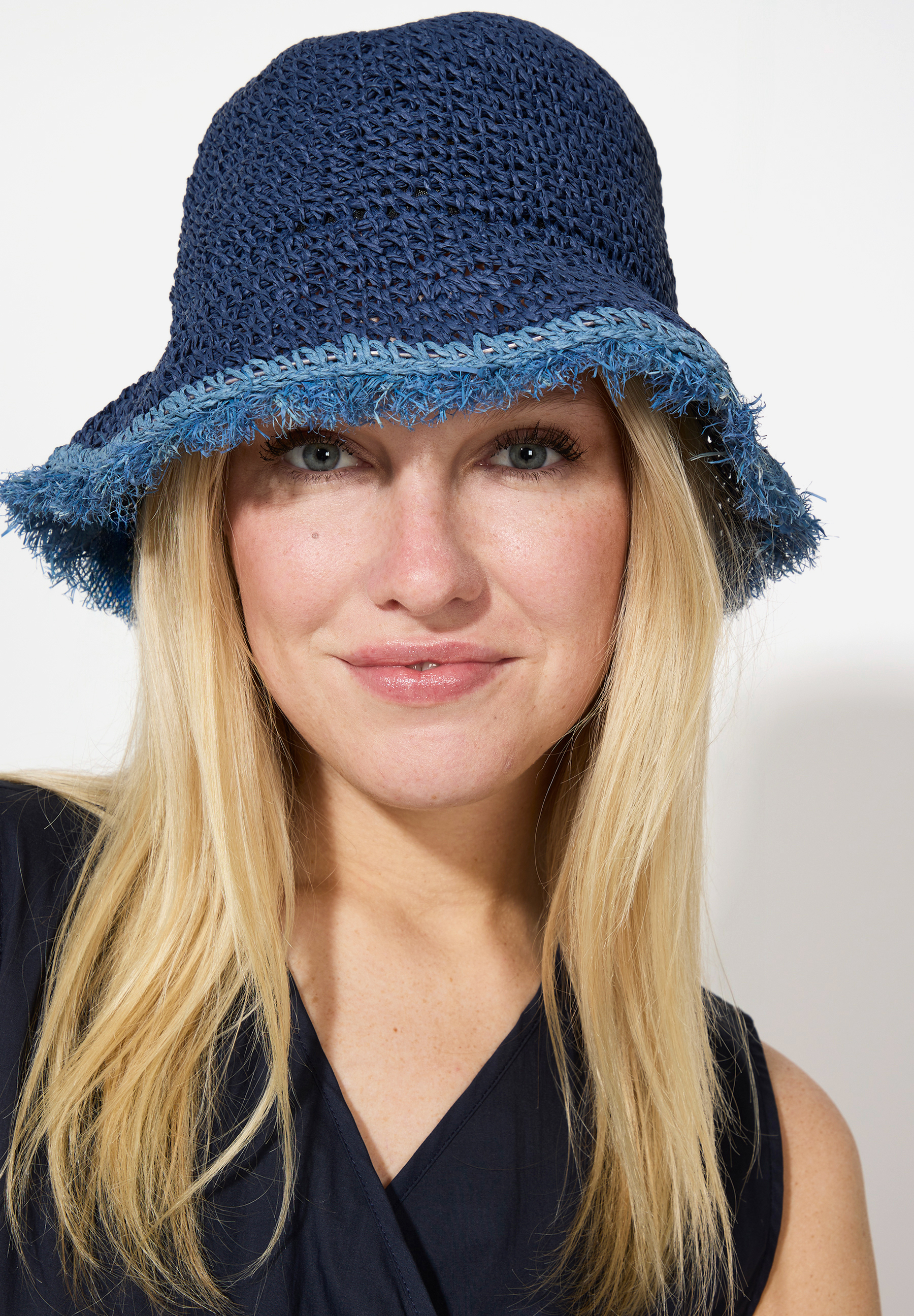 Eine Frau mit blonden Haaren und einem blauen MORE & MORE-Hut blickt in die Kamera.