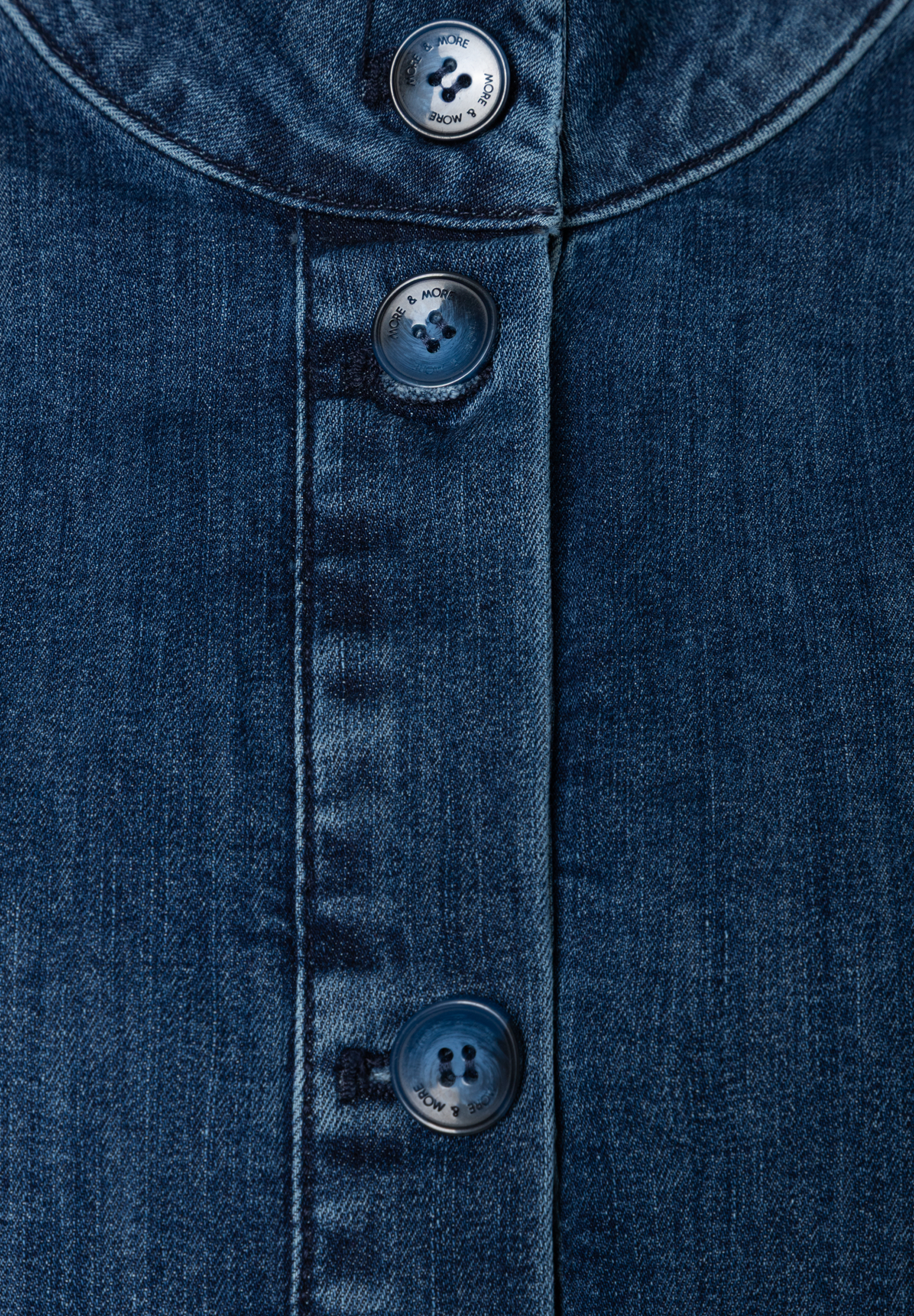 Nahaufnahme eines blauen MORE & MORE Oberteils aus Denim mit Knöpfen. Nahaufnahme eines blauen MORE & MORE Oberteils aus Denim mit Knöpfen.
