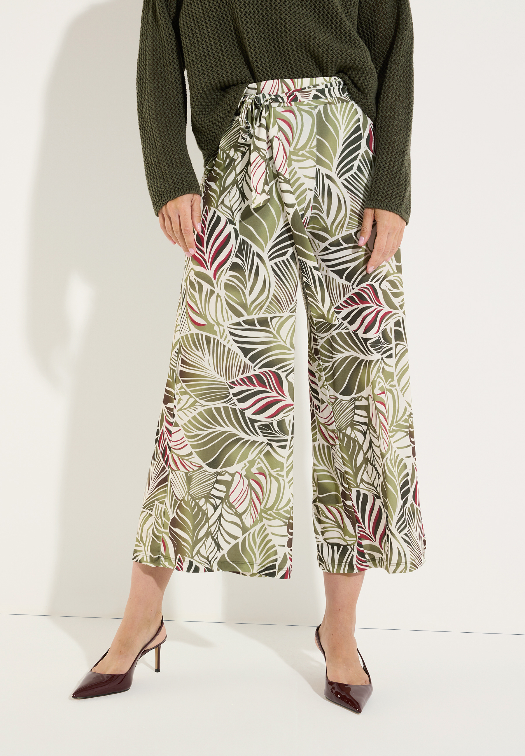 MORE & MORE Jersey-Hose mit Palmenmuster in Grün, Weiß & Rot, kombiniert mit weißen Sandalen.