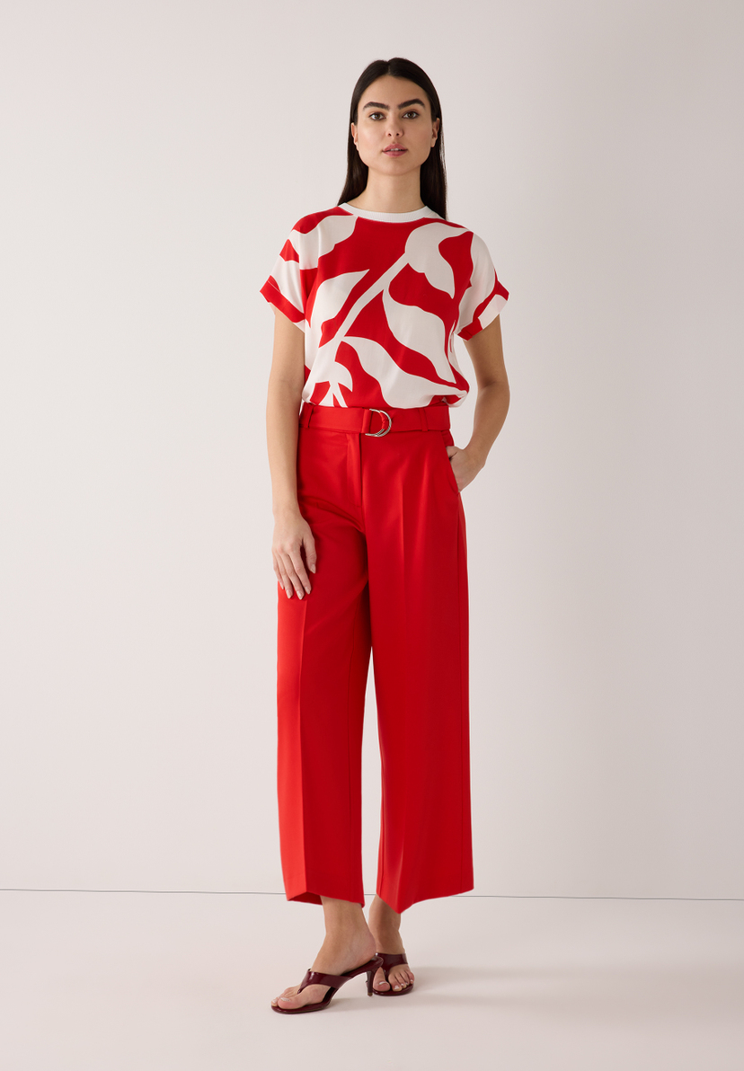 Eine Frau, die ein rotes und weißes Outfit von MORE & MORE trägt, posiert vor einer weißen Wand. Eine Frau, die ein rotes und weißes Outfit von MORE & MORE trägt, posiert vor einer weißen Wand.