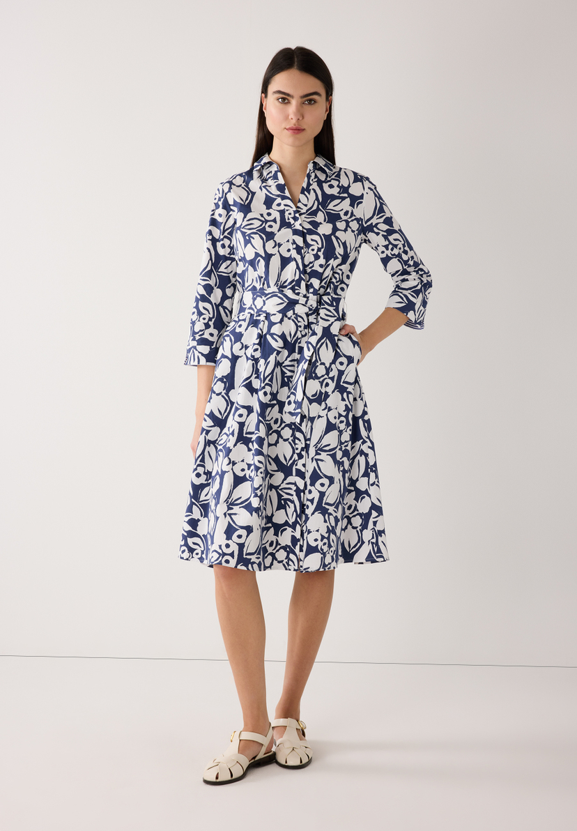 Eine Frau mit einem blau-weißen MORE & MORE Kleid mit floralem Muster und Gürtel. Eine Frau mit einem blau-weißen MORE & MORE Kleid mit floralem Muster und Gürtel.