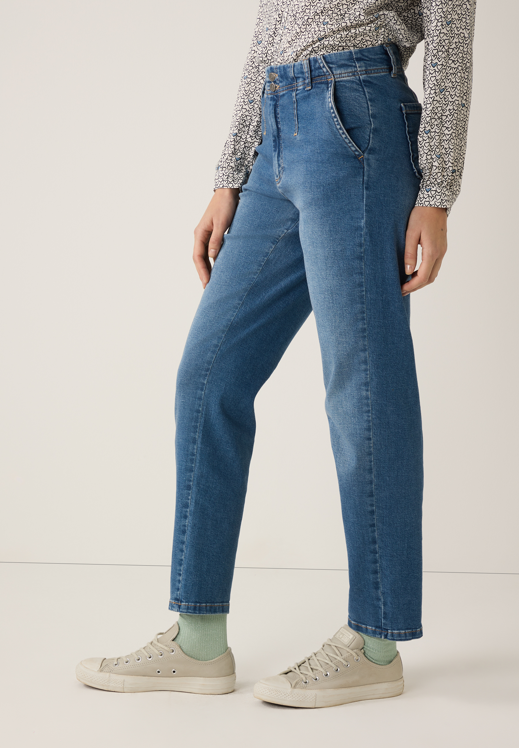 Nahaufnahme einer Person in MORE & MORE Jeans und Sneakers vor hellem Hintergrund. Nahaufnahme einer Person in MORE & MORE Jeans und Sneakers vor hellem Hintergrund.