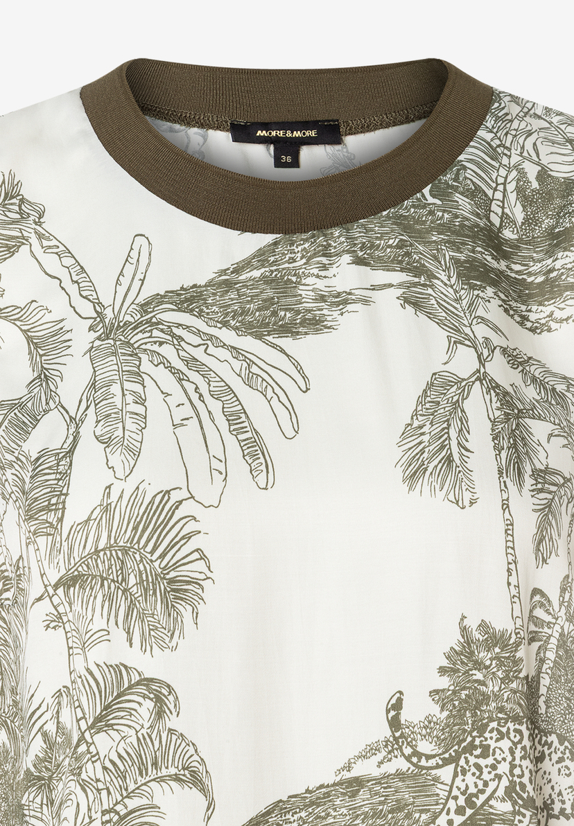 Nahaufnahme einer MORE & MORE Bluse mit Dschungel-Print und olivfarbenem Rundhals-Ausschnitt. Nahaufnahme einer MORE & MORE Bluse mit Dschungel-Print und olivfarbenem Rundhals-Ausschnitt.