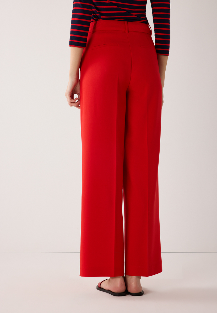 Rückansicht einer Frau in roter, fließender Webware Hose von MORE & MORE mit marineblau-rot gestreiftem Oberteil. Rückansicht einer Frau in roter, fließender Webware Hose von MORE & MORE mit marineblau-rot gestreiftem Oberteil.
