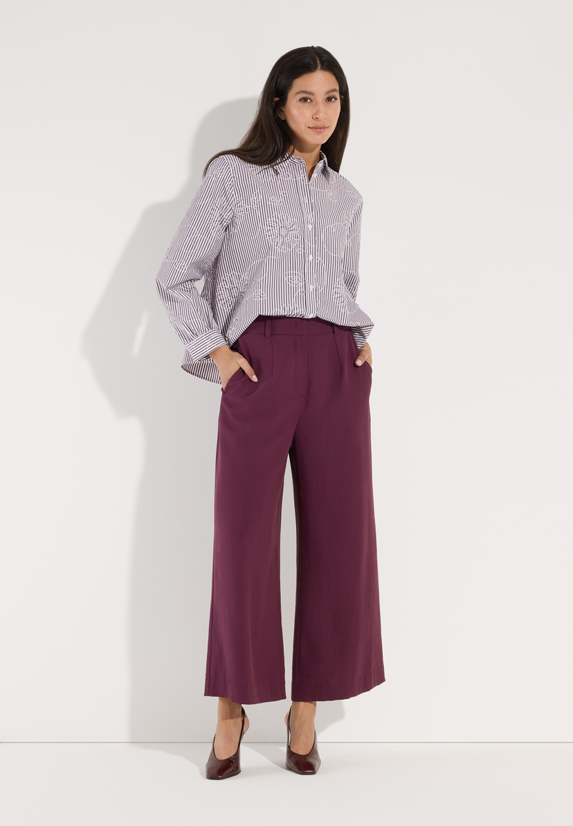 MORE & MORE Bluse: Eine Frau trägt eine gestreifte Bluse mit Blumenmuster und weinroter Culotte, Hände in Taschen. MORE & MORE Bluse: Eine Frau trägt eine gestreifte Bluse mit Blumenmuster und weinroter Culotte, Hände in Taschen.