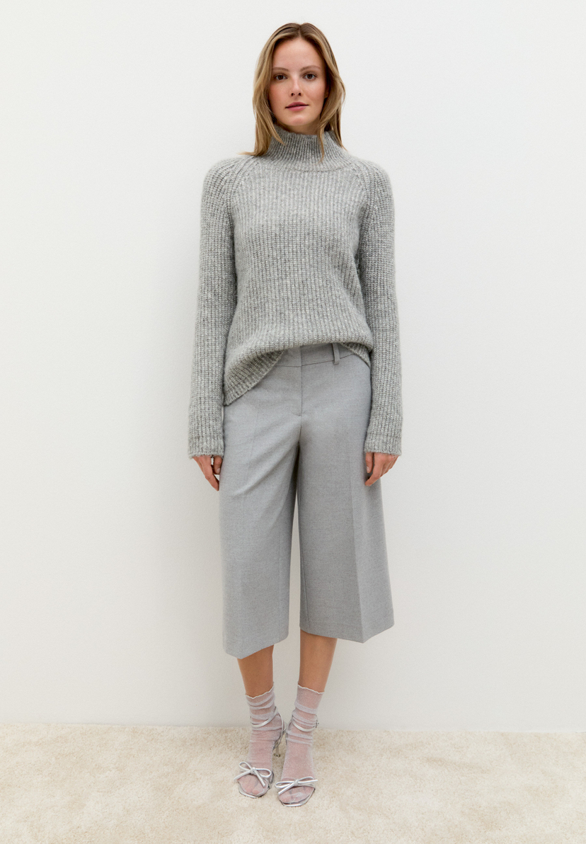 Eine Frau trägt einen grauen MORE & MORE Strickpullover, graue Culottes und silberne Sandalen mit Schleife. Eine Frau trägt einen grauen MORE & MORE Strickpullover, graue Culottes und silberne Sandalen mit Schleife.
