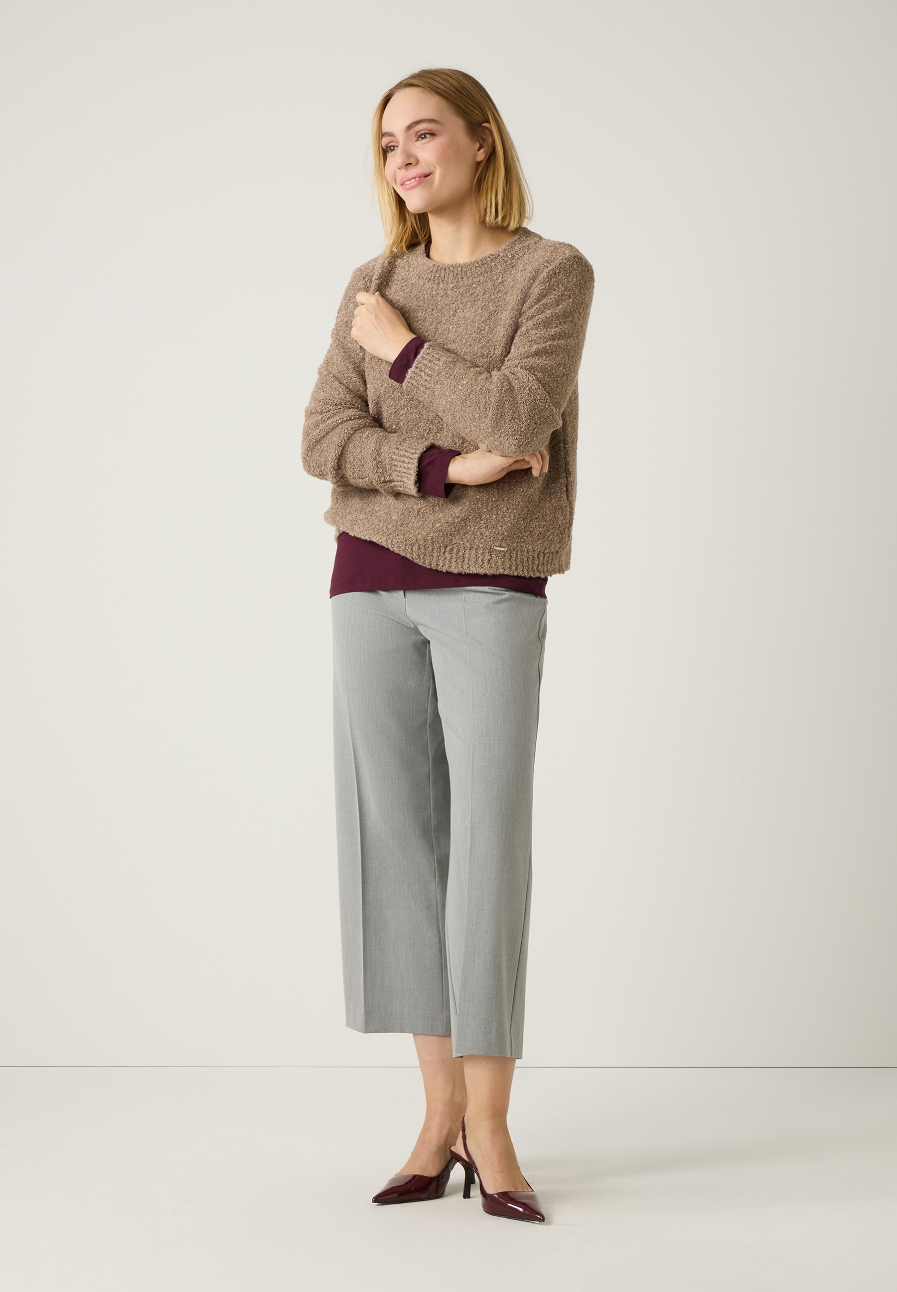 Eine Frau mit einem beigen MORE & MORE Strick-Bouclé-Pullover und grauer Hose. Angenehmer, warmer Tragekomfort. Eine Frau mit einem beigen MORE & MORE Strick-Bouclé-Pullover und grauer Hose. Angenehmer, warmer Tragekomfort.