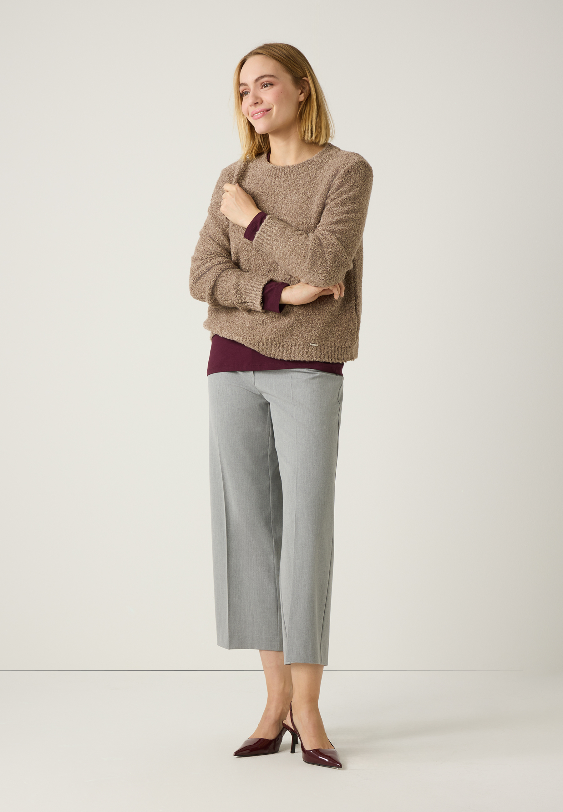 Eine Frau mit einem beigen MORE & MORE Strick-Bouclé-Pullover und grauer Hose. Angenehmer, warmer Tragekomfort. Eine Frau mit einem beigen MORE & MORE Strick-Bouclé-Pullover und grauer Hose. Angenehmer, warmer Tragekomfort.