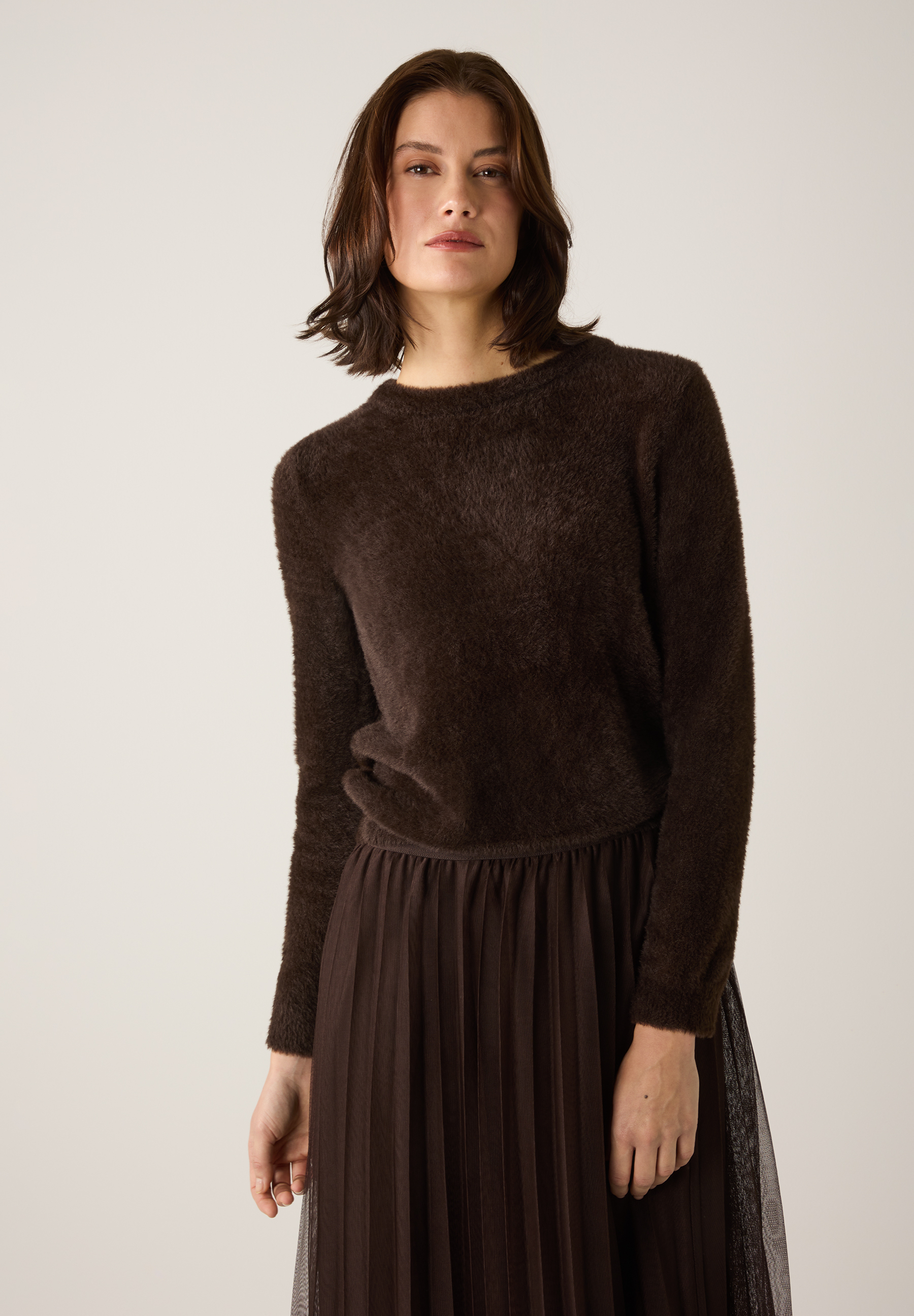 Eine Frau trägt einen braunen MORE & MORE Strickpullover mit angenehmen Tragekomfort und dazu einen passenden Rock.