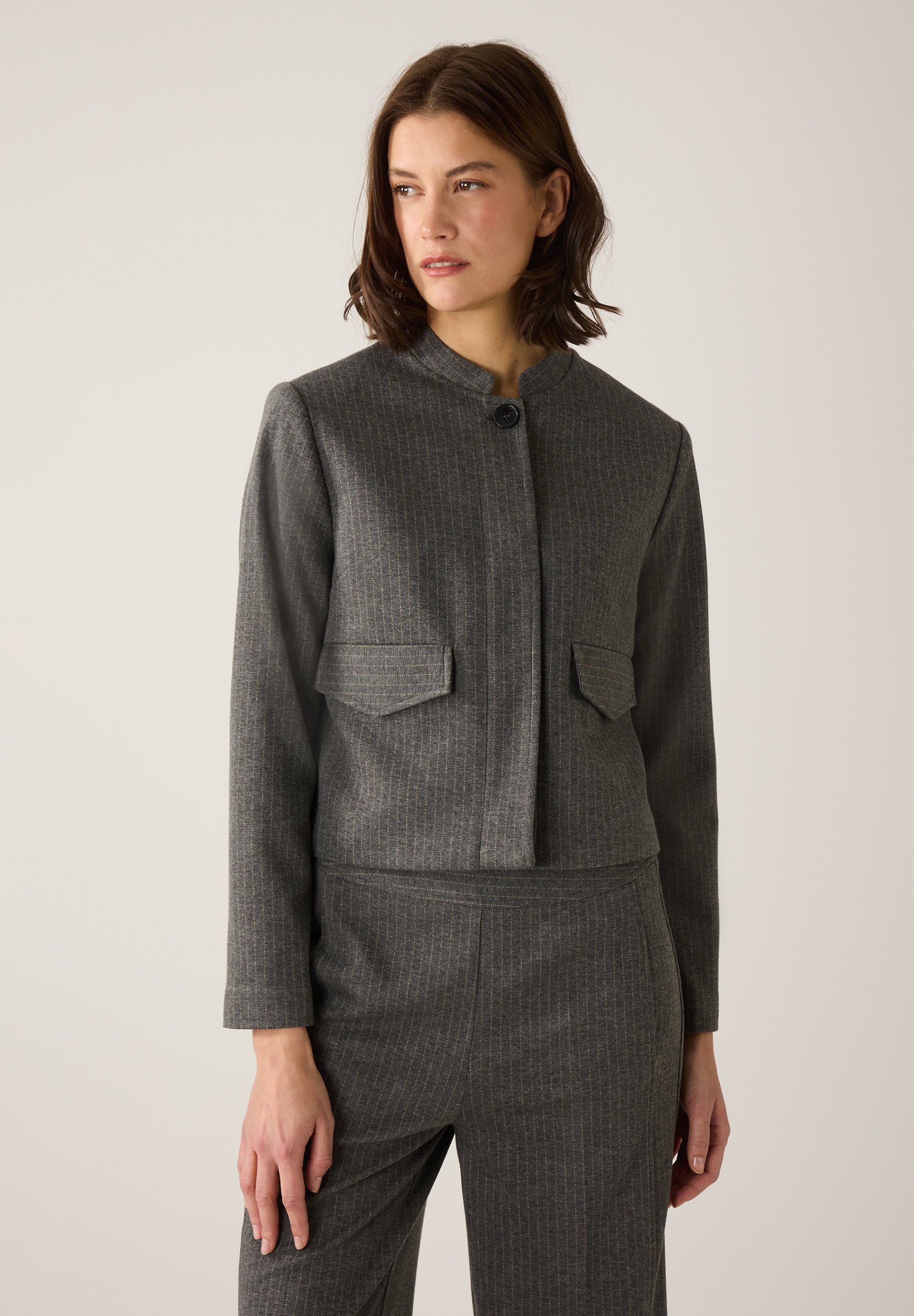 Eine Frau trägt einen grauen Nadelstreifen-Blazer von MORE & MORE und eine passende Hose.