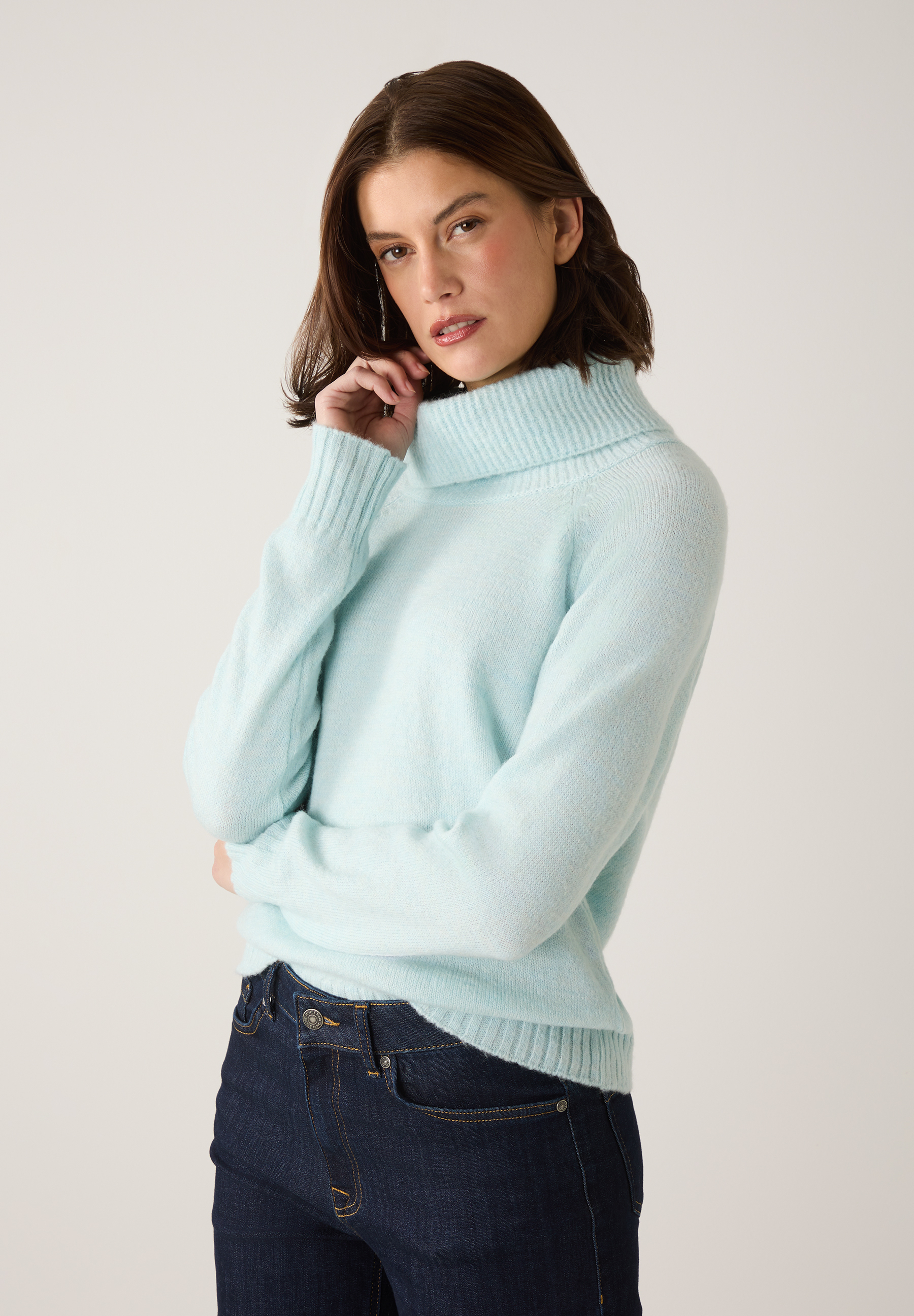 Eine Frau trägt einen hellblauen Strick-Rollkragenpullover von MORE & MORE und eine dunkle Jeans.