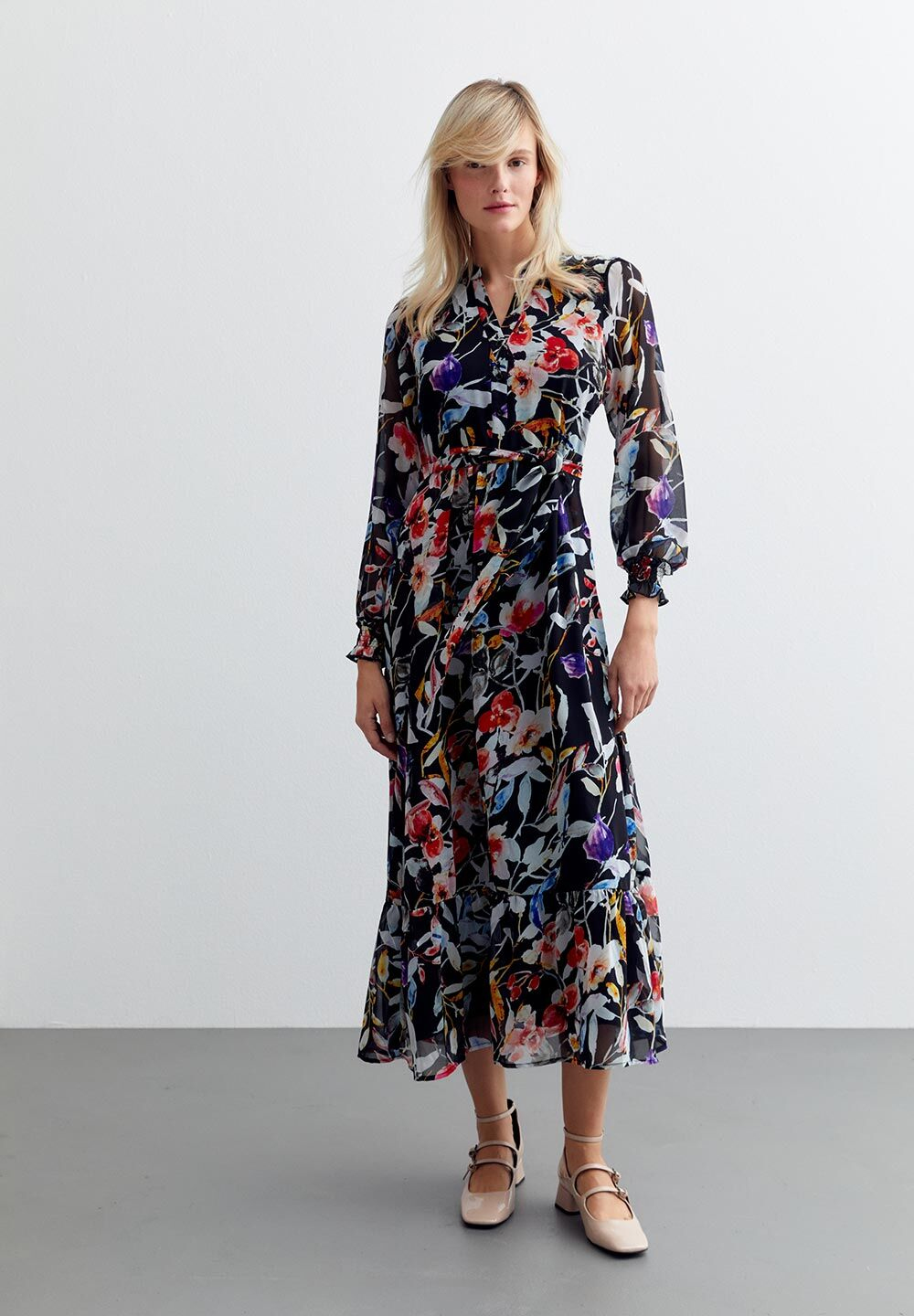 Eine Frau trägt ein schwarzes, blumiges MORE & MORE Chiffon-Oberteil, ein Kleid mit langen Ärmeln und passenden Schuhen.