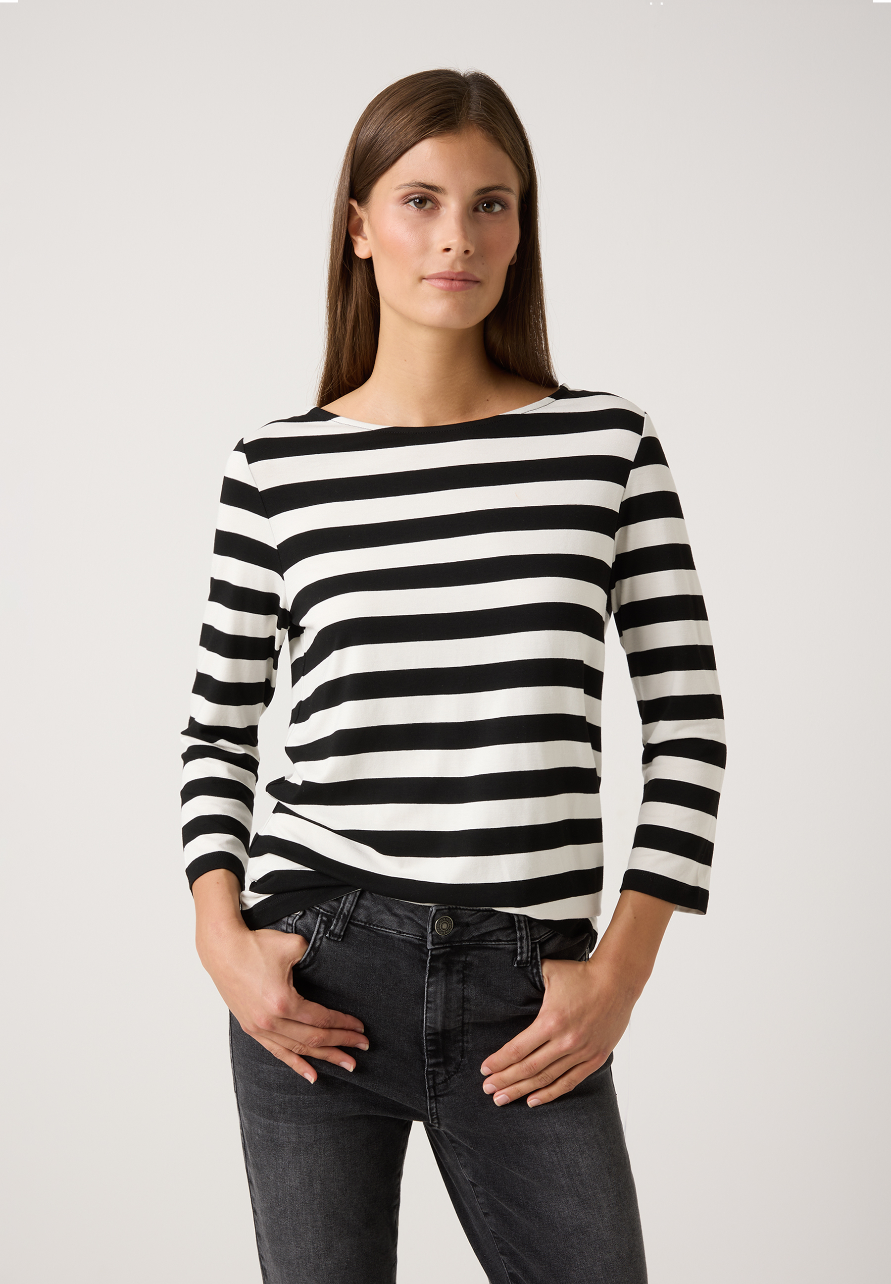 Eine Frau präsentiert ein MORE & MORE Oberteil mit schwarzen und weißen Streifen, kombiniert mit dunklen Jeans.