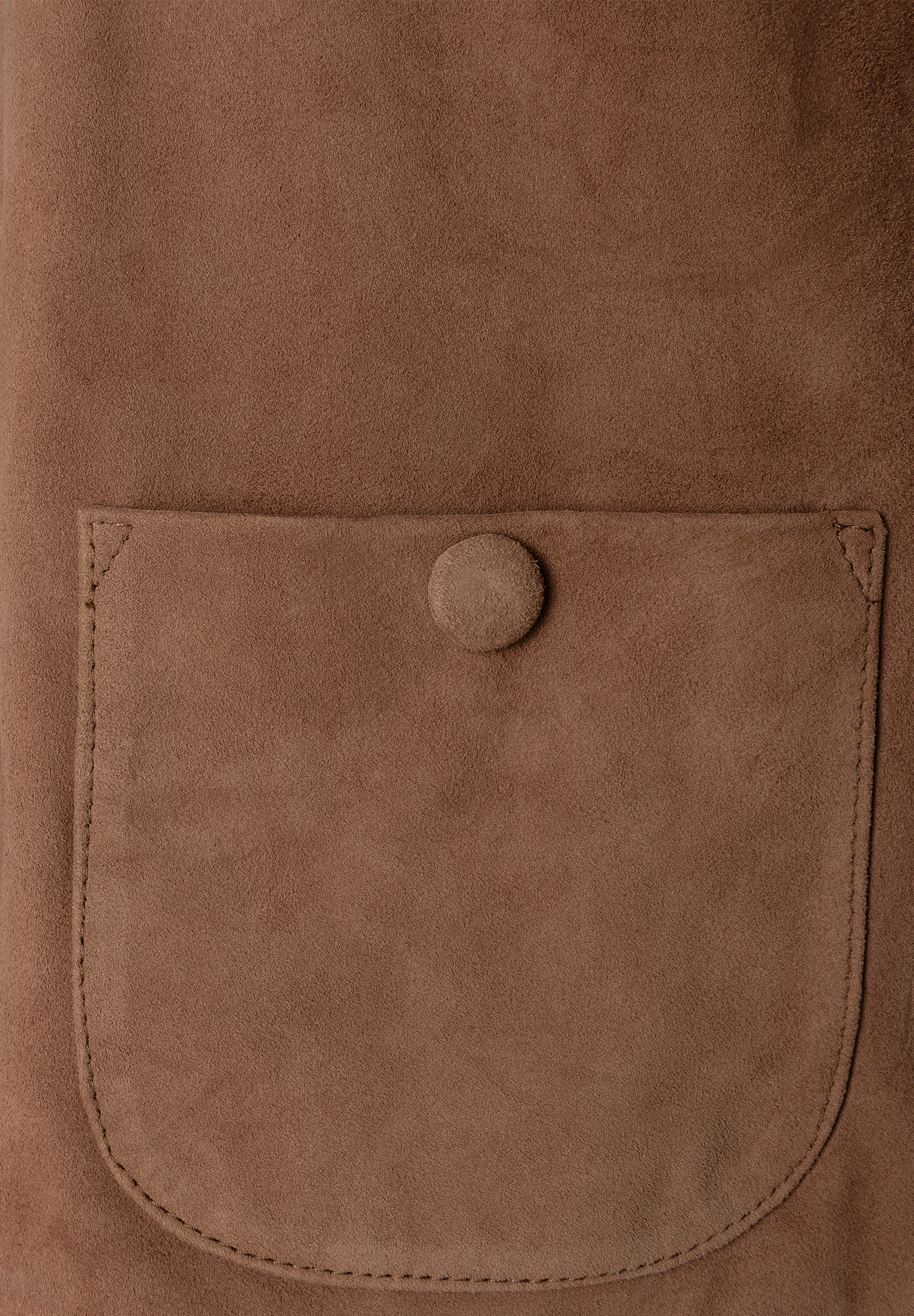 Nahaufnahme eines MORE & MORE Oberteils aus braunem Veloursleder mit aufgesetzter Tasche und Knopf. Nahaufnahme eines MORE & MORE Oberteils aus braunem Veloursleder mit aufgesetzter Tasche und Knopf.