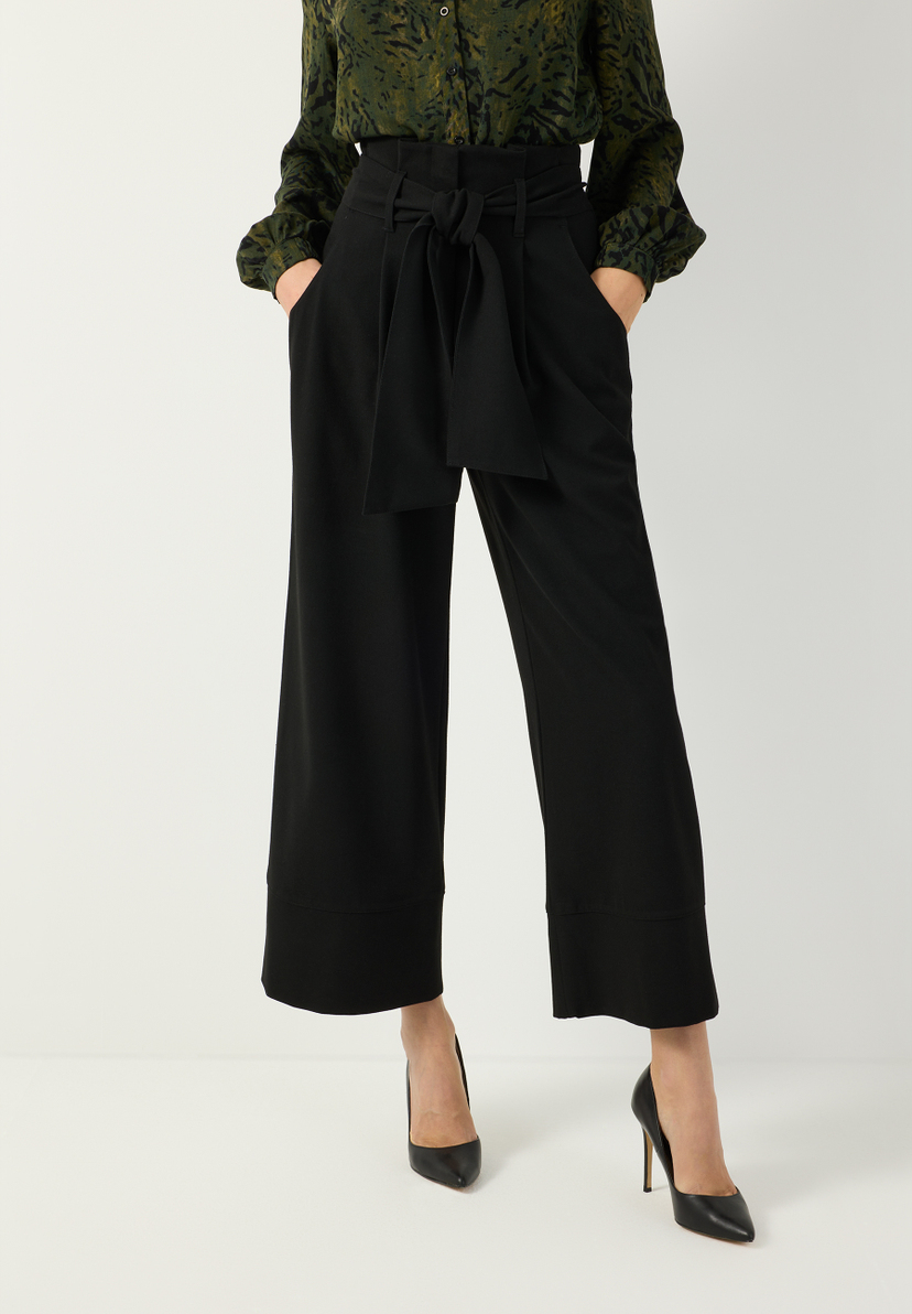 MORE & MORE schwarze Palazzo-Hose mit hohem Bund und Bindegürtel, dazu dunkelgrüne Bluse mit Muster und schwarzen Pumps. MORE & MORE schwarze Palazzo-Hose mit hohem Bund und Bindegürtel, dazu dunkelgrüne Bluse mit Muster und schwarzen Pumps.