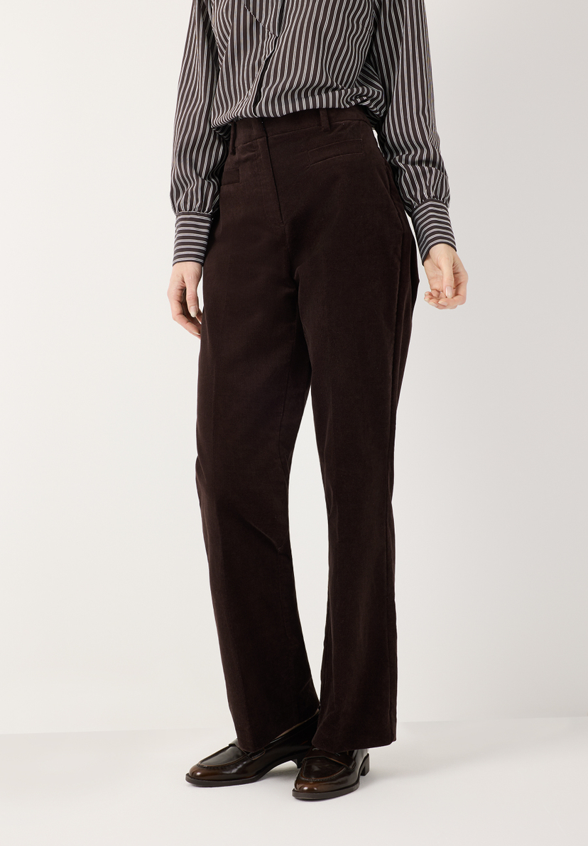 MORE & MORE Cordhose in Dunkelbraun, kombiniert mit gestreifter Bluse und glänzenden Loafers auf hellem Grund.