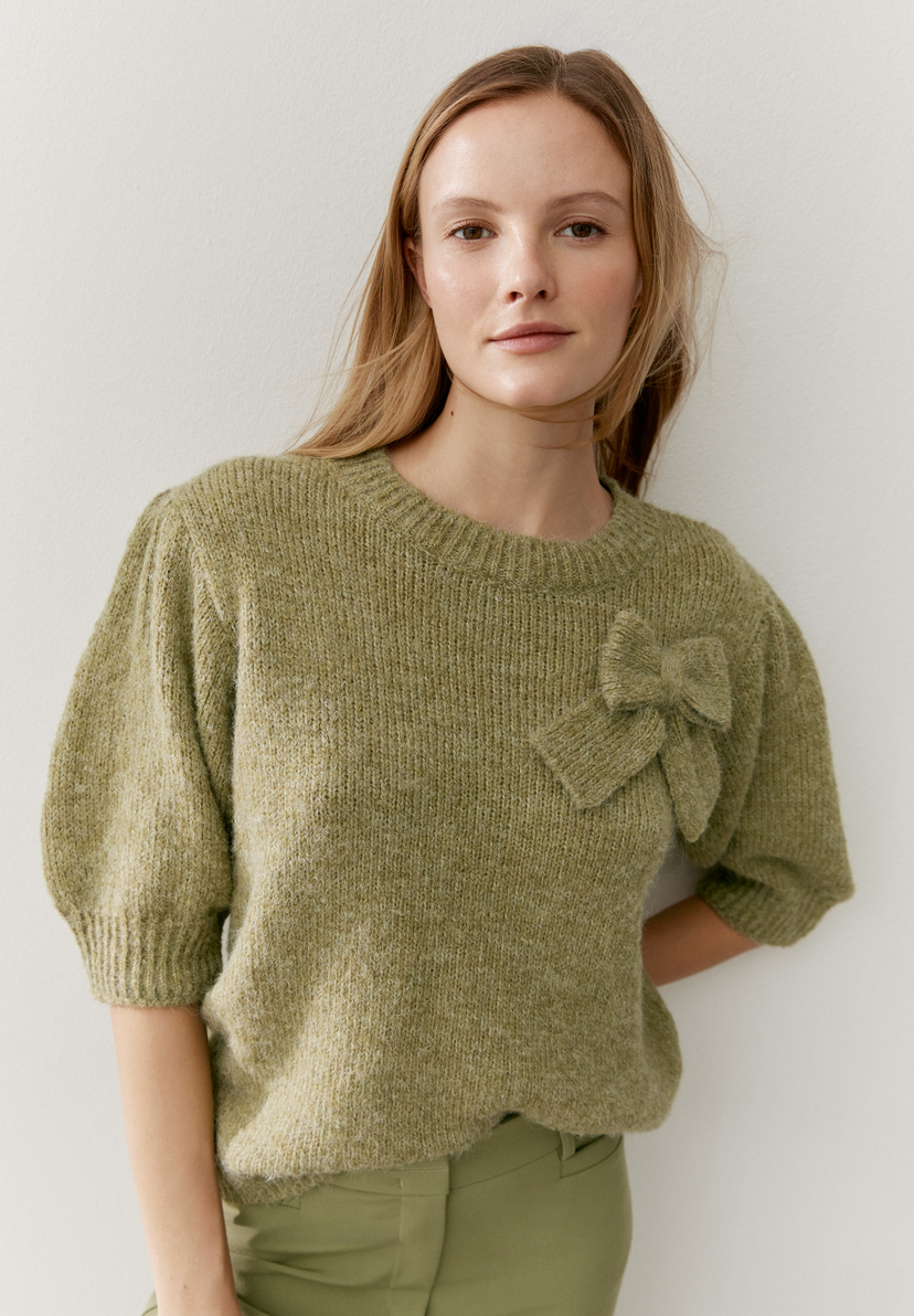 Eine Frau trägt einen grünen Strickpullover mit Schleife von MORE & MORE. Eine Frau trägt einen grünen Strickpullover mit Schleife von MORE & MORE.