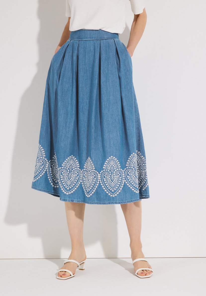 Ein MORE & MORE Rock aus Denim mit weißem Muster am Saum, kombiniert mit weißen Sandalen. Ein MORE & MORE Rock aus Denim mit weißem Muster am Saum, kombiniert mit weißen Sandalen.