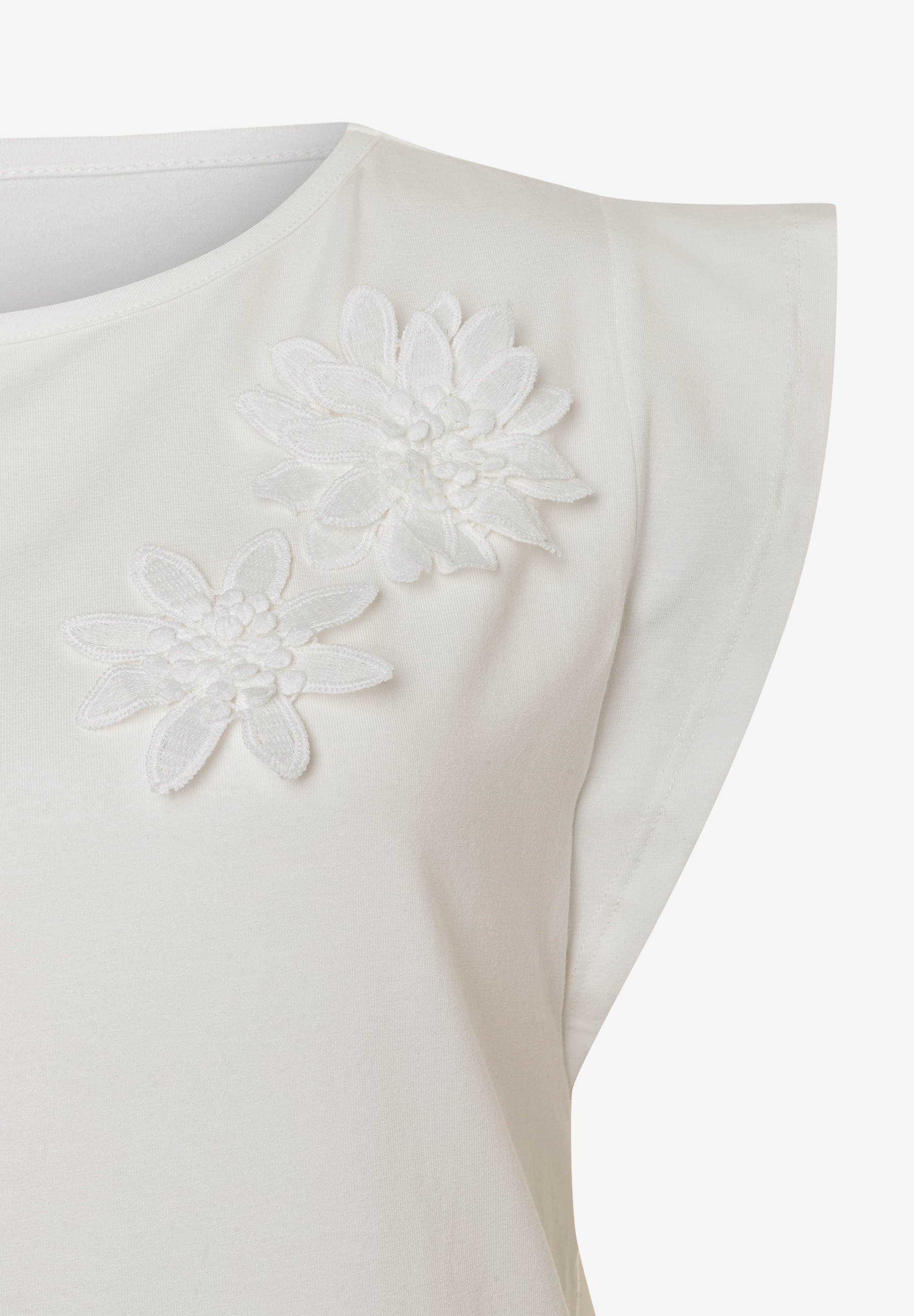 Detailaufnahme eines MORE & MORE T-Shirts, weiß, mit zwei applizierten weißen Blüten. Detailaufnahme eines MORE & MORE T-Shirts, weiß, mit zwei applizierten weißen Blüten.