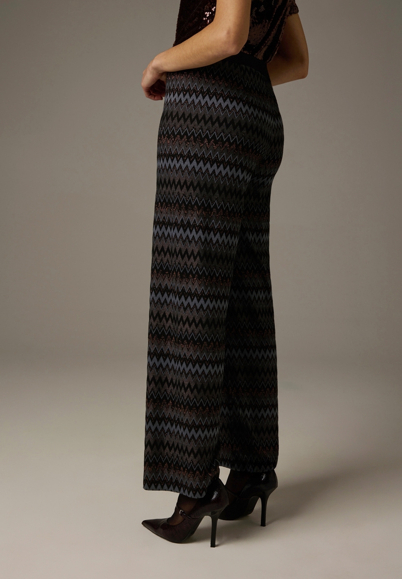 Eine Frau in MORE & MORE Jersey-Hosen/Jeans mit Zickzackmuster und High Heels, seitliche Ansicht. Eine Frau in MORE & MORE Jersey-Hosen/Jeans mit Zickzackmuster und High Heels, seitliche Ansicht.