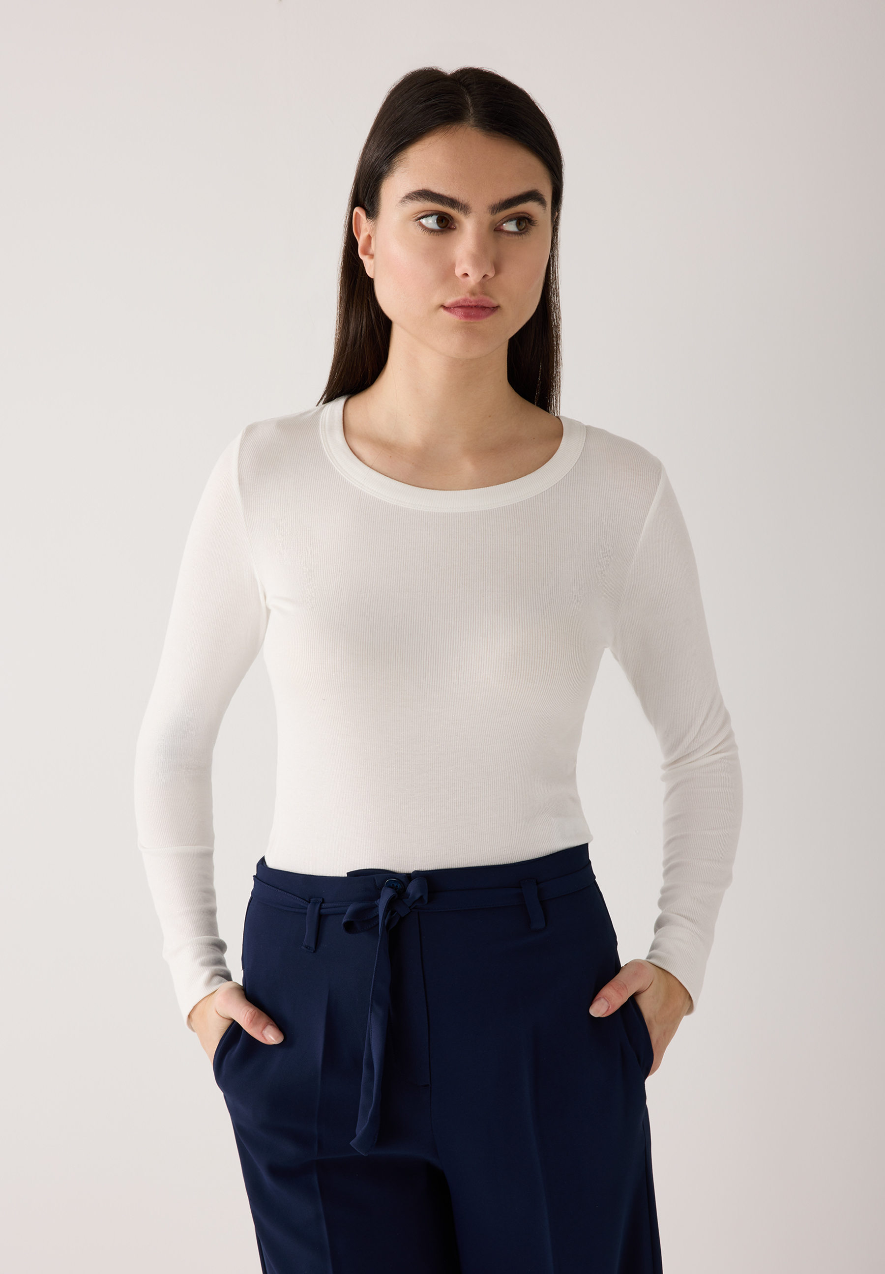 Eine Frau mit MORE & MORE Oberteil. Das gerippte Shirt hat lange Ärmel und wird mit einer blauen Hose kombiniert. Angenehmer Tragekomfort.