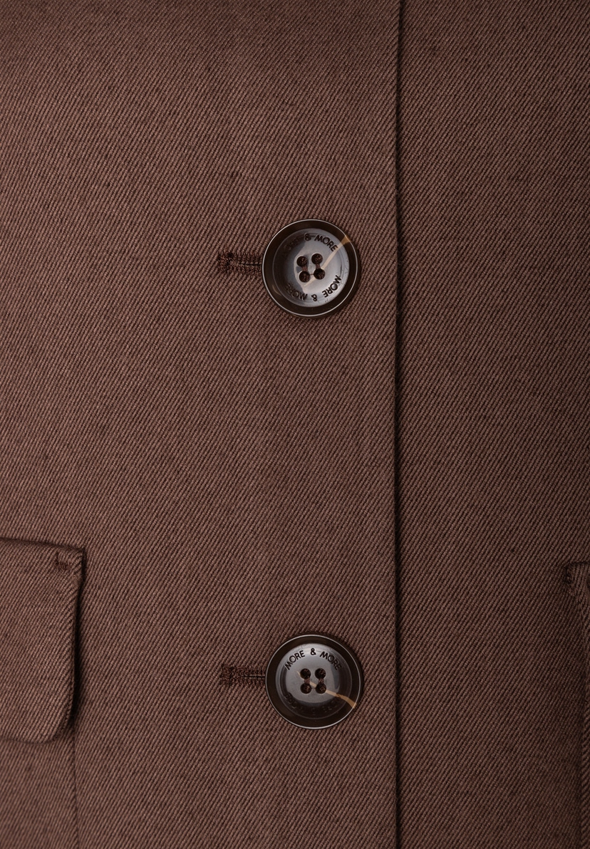Nahaufnahme des braunen MORE & MORE Blazers: zwei runde, braune Knöpfe mit Markenlogo, die diagonal angeordnet sind. Nahaufnahme des braunen MORE & MORE Blazers: zwei runde, braune Knöpfe mit Markenlogo, die diagonal angeordnet sind.