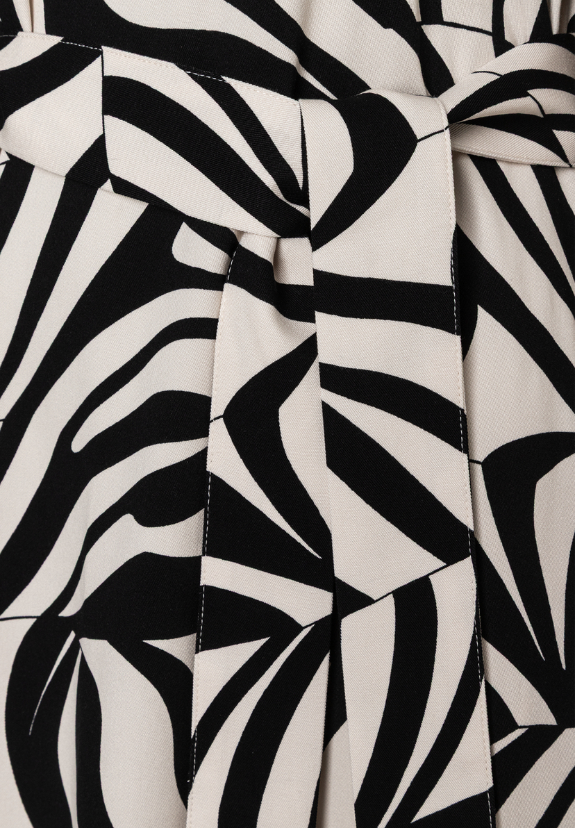 Nahaufnahme eines MORE & MORE Oberteils mit abstraktem, schwarz-weißem Muster und einem Bindegürtel in der Taille. Nahaufnahme eines MORE & MORE Oberteils mit abstraktem, schwarz-weißem Muster und einem Bindegürtel in der Taille.