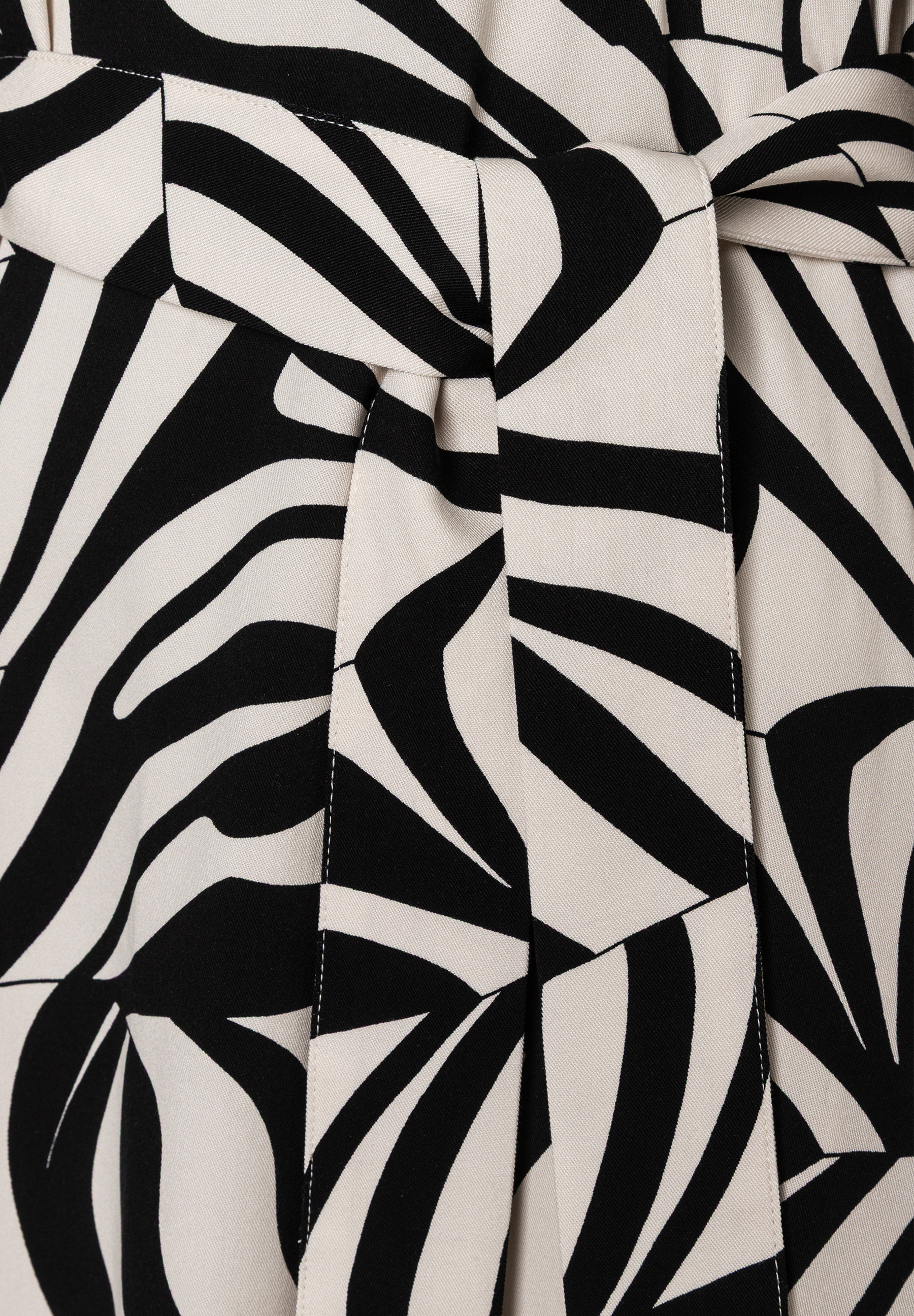 Nahaufnahme eines MORE & MORE Oberteils mit abstraktem, schwarz-weißem Muster und einem Bindegürtel in der Taille. Nahaufnahme eines MORE & MORE Oberteils mit abstraktem, schwarz-weißem Muster und einem Bindegürtel in der Taille.