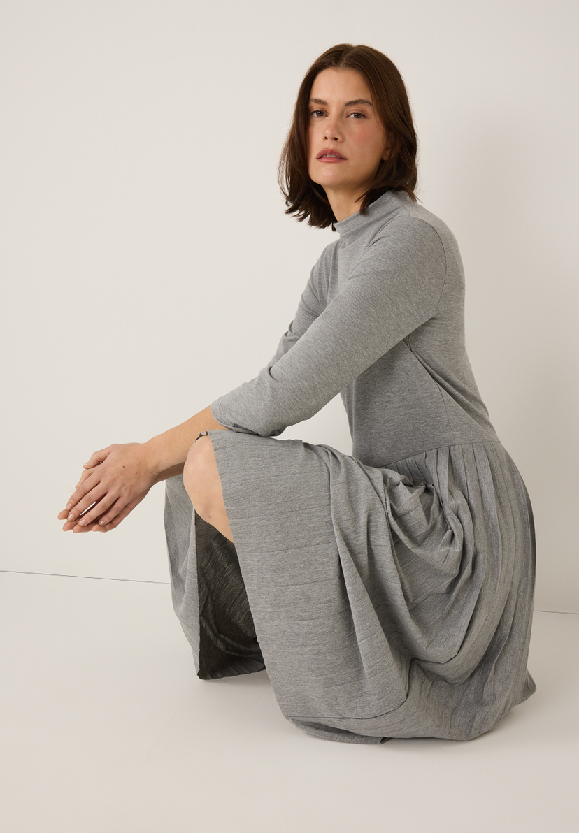 Eine Frau hockt in einem grauen MORE & MORE Jersey-Oberteil mit langen Ärmeln. Eine Frau hockt in einem grauen MORE & MORE Jersey-Oberteil mit langen Ärmeln.