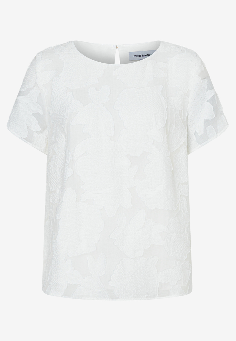Eine weiße, kurzärmelige MORE & MORE Bluse mit einem floralen Muster auf weißem Hintergrund. Eine weiße, kurzärmelige MORE & MORE Bluse mit einem floralen Muster auf weißem Hintergrund.
