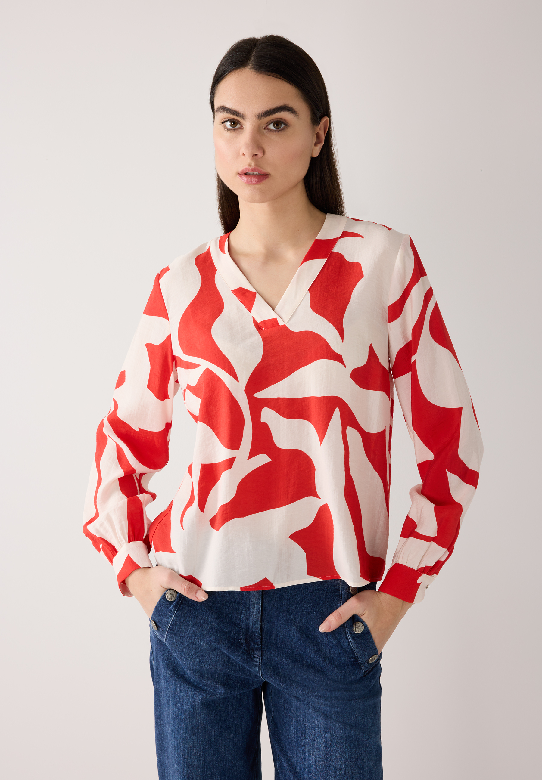 Eine Frau, die eine MORE & MORE Bluse mit rotem Muster trägt. Eine Frau, die eine MORE & MORE Bluse mit rotem Muster trägt.