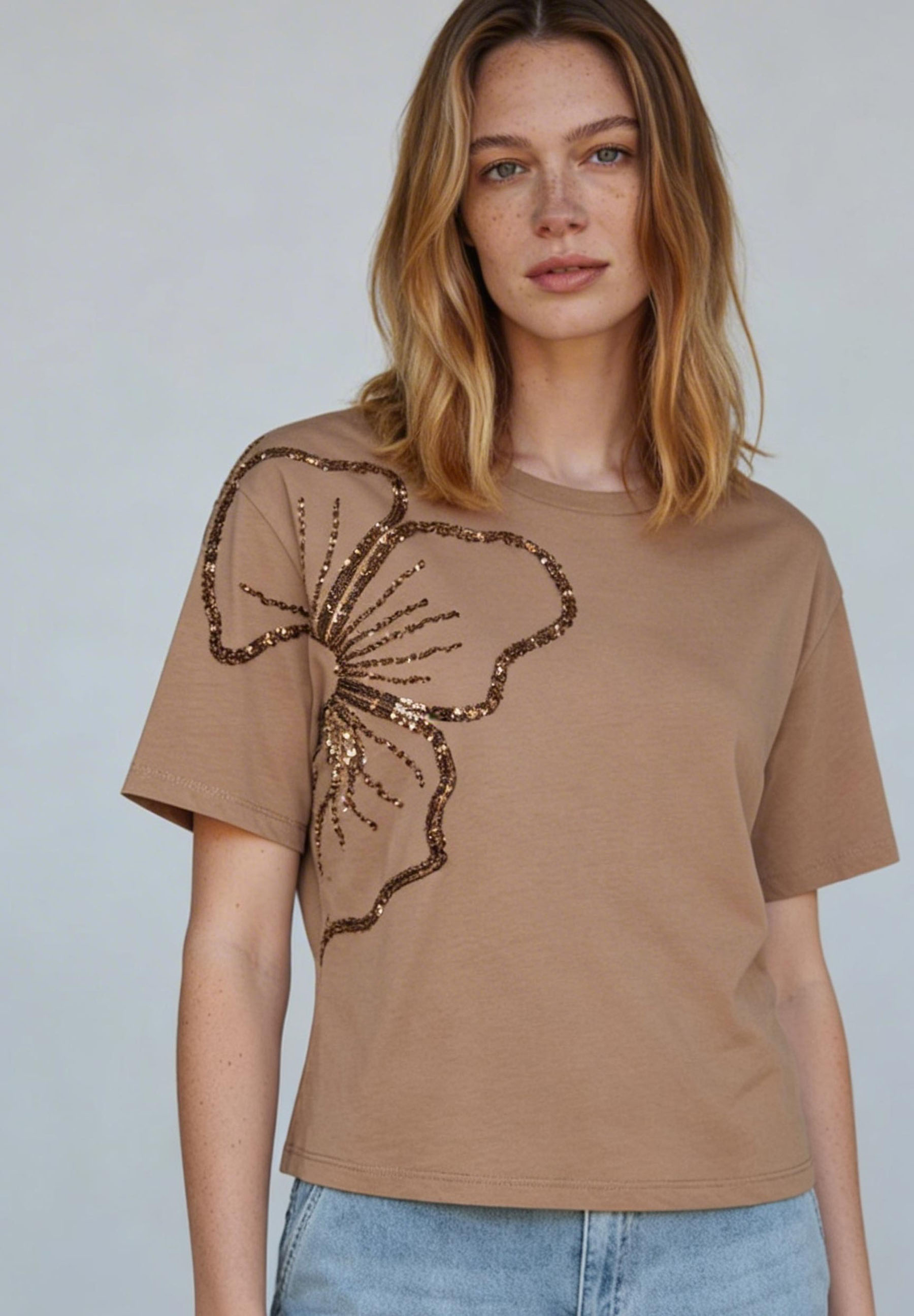 Eine Frau trägt ein MORE & MORE T-Shirt mit Jersey-Struktur und einer glitzernden Blumenapplikation.