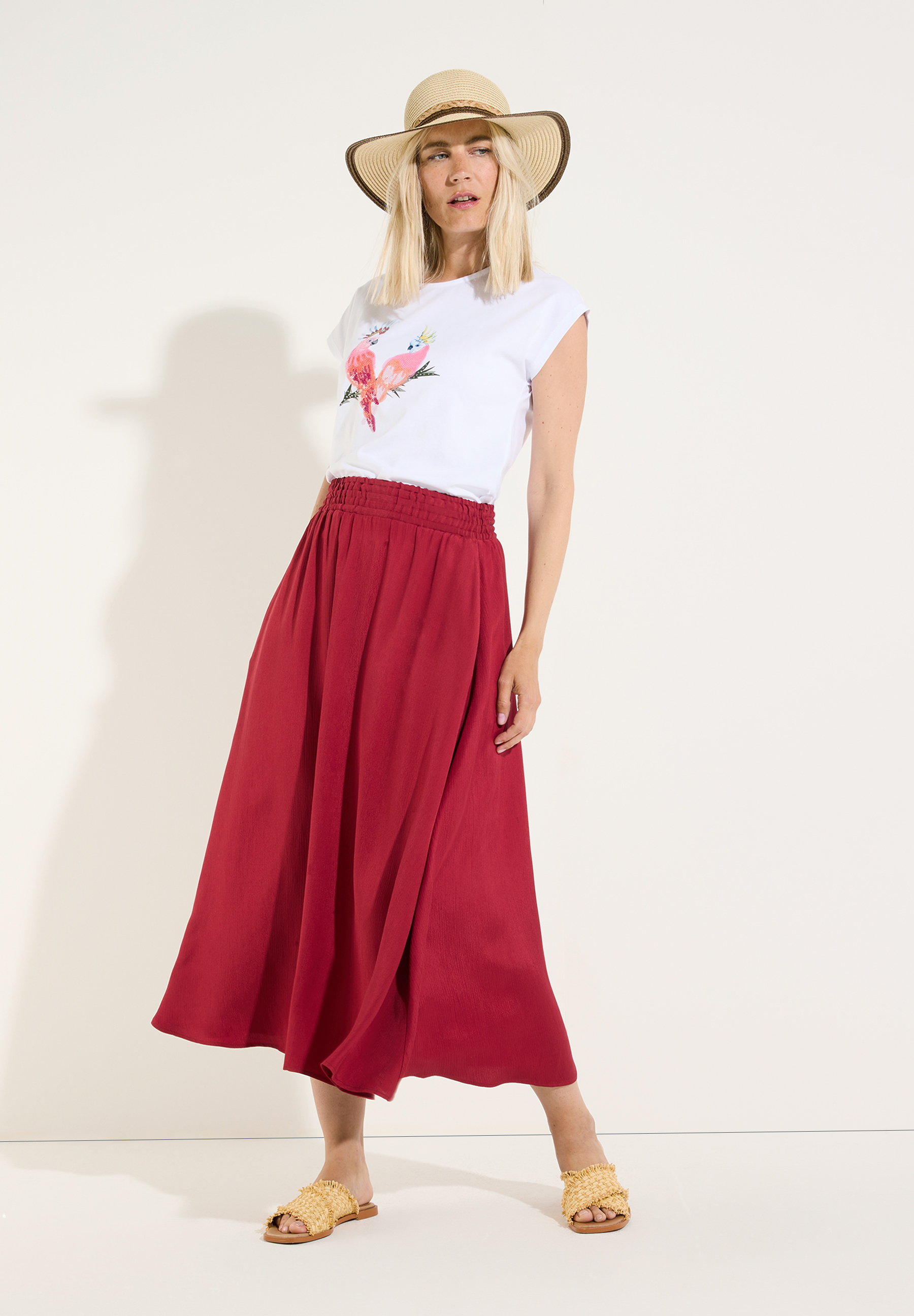 MORE & MORE T-Shirt mit Papageien-Print und rotem Rock, Strohhut, Stroh-Sandalen MORE & MORE T-Shirt mit Papageien-Print und rotem Rock, Strohhut, Stroh-Sandalen