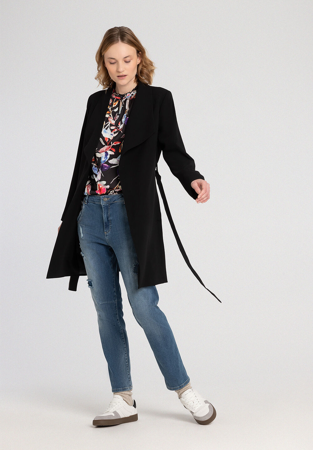Eine Frau in MORE & MORE Jeans und schwarzem Mantel posiert vor einem neutralen Hintergrund. Eine Frau in MORE & MORE Jeans und schwarzem Mantel posiert vor einem neutralen Hintergrund.