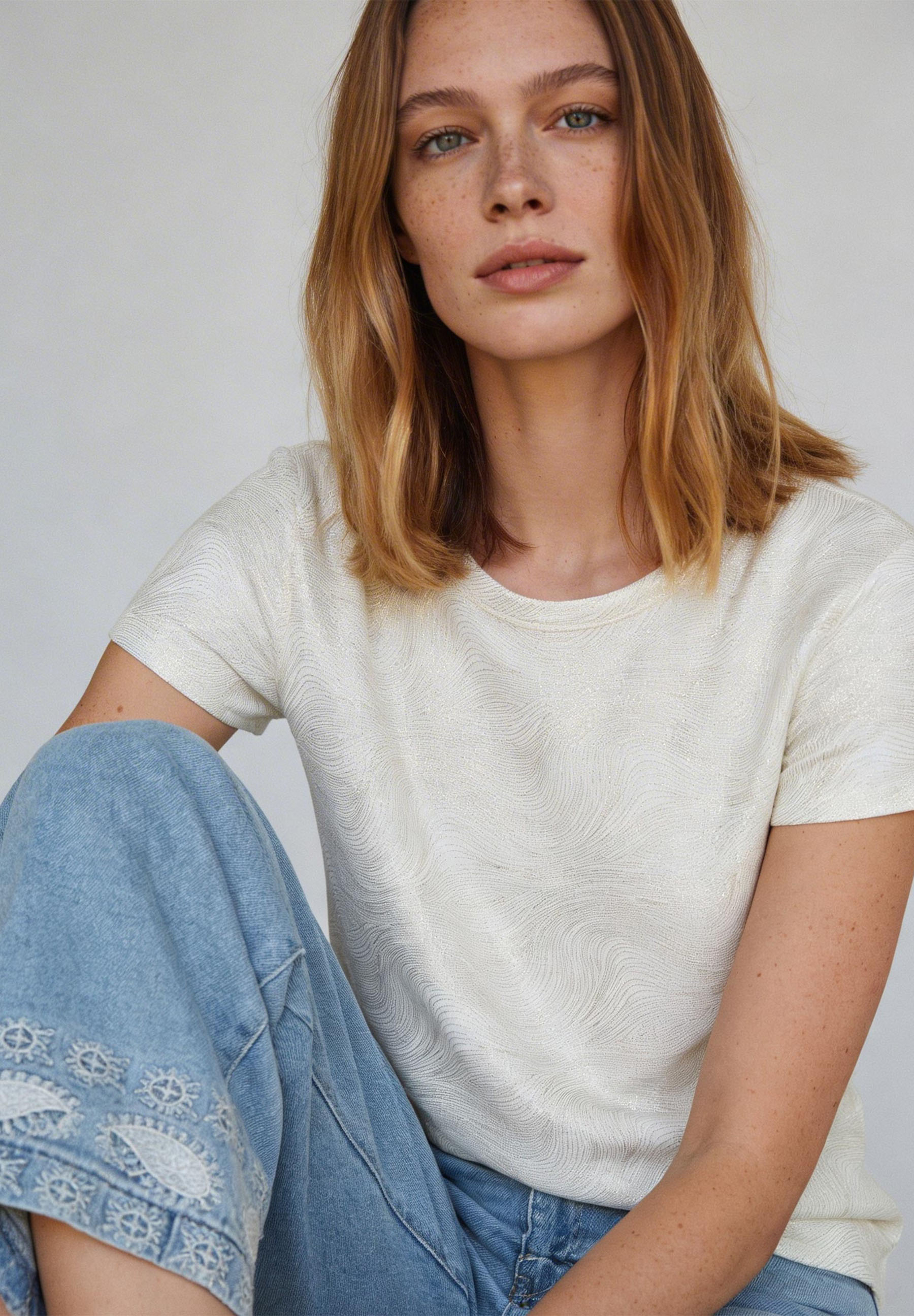 AI generated - Eine Frau mit Sommersprossen trägt ein weißes MORE & MORE Jersey-Oberteil und Jeans. AI generated - Eine Frau mit Sommersprossen trägt ein weißes MORE & MORE Jersey-Oberteil und Jeans.