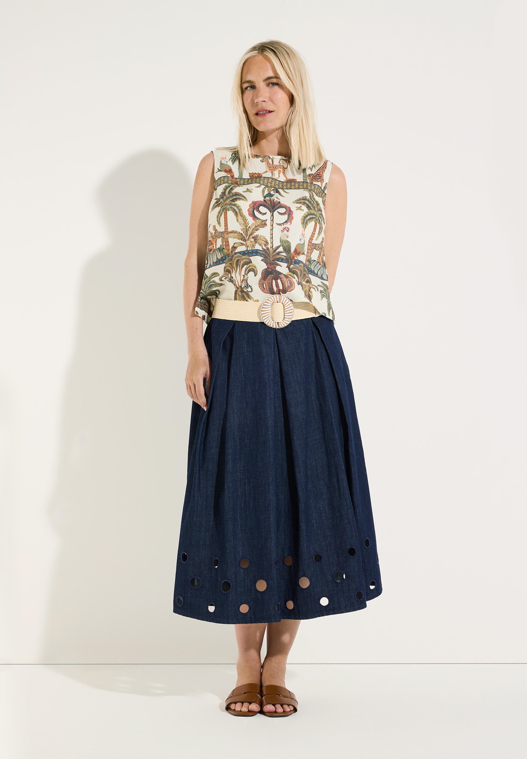 MORE & MORE Bluse: Eine Frau trägt eine ärmellose Bluse mit Dschungelmotiv und einen dunkelblauen Rock mit Lochmuster am Saum. MORE & MORE Bluse: Eine Frau trägt eine ärmellose Bluse mit Dschungelmotiv und einen dunkelblauen Rock mit Lochmuster am Saum.