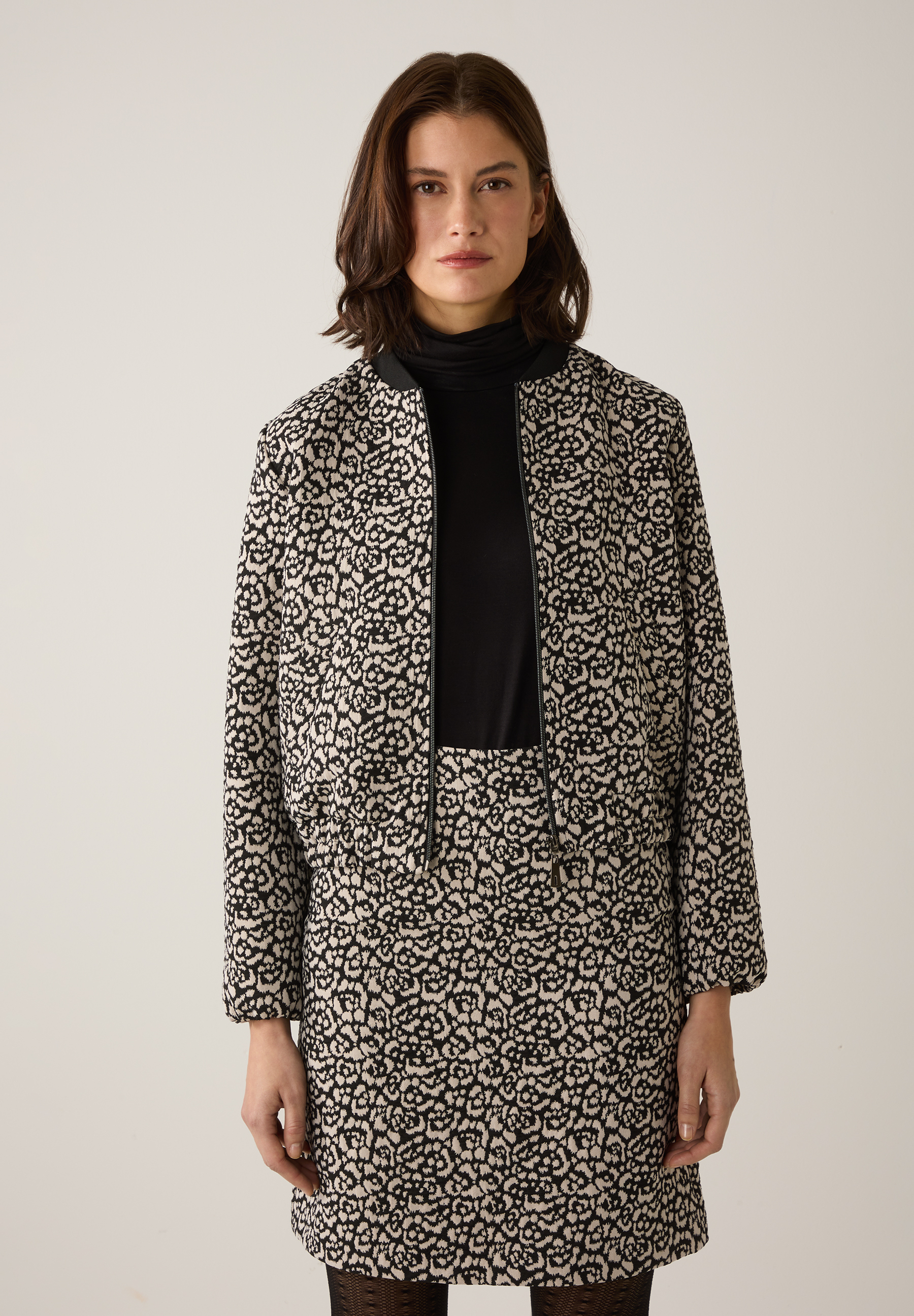 Eine Frau mit MORE & MORE Blazer und passendem Rock mit floralem Muster.