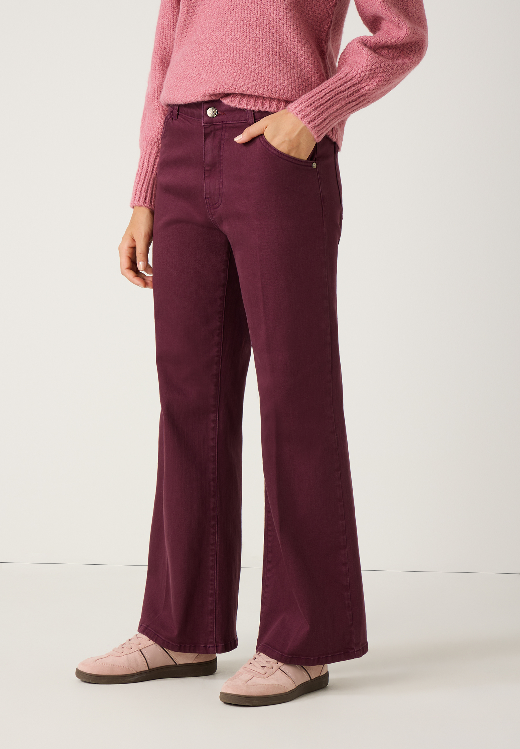 Eine Frau, die eine bordeauxrote Schlaghose von MORE & MORE und dazu einen rosa Pullover und passende Schuhe trägt. Eine Frau, die eine bordeauxrote Schlaghose von MORE & MORE und dazu einen rosa Pullover und passende Schuhe trägt.