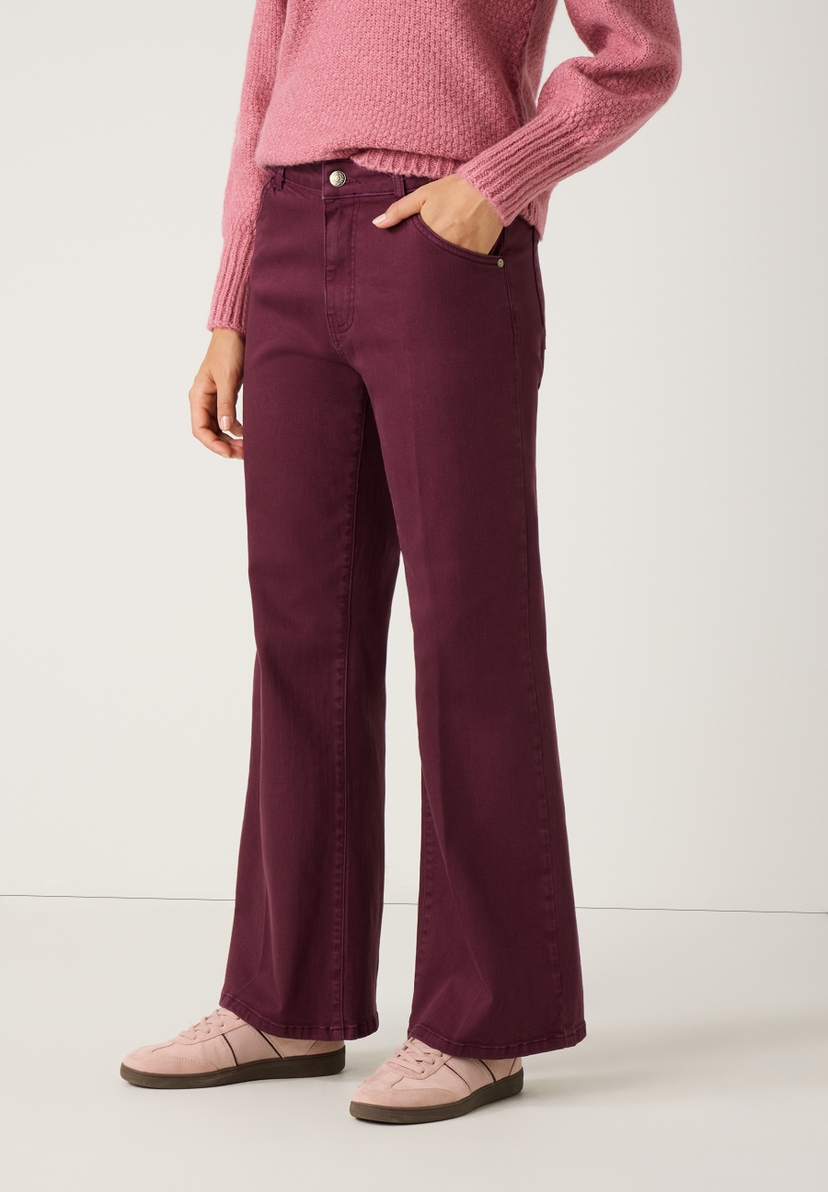Eine Frau, die eine bordeauxrote Schlaghose von MORE & MORE und dazu einen rosa Pullover und passende Schuhe trägt. Eine Frau, die eine bordeauxrote Schlaghose von MORE & MORE und dazu einen rosa Pullover und passende Schuhe trägt.
