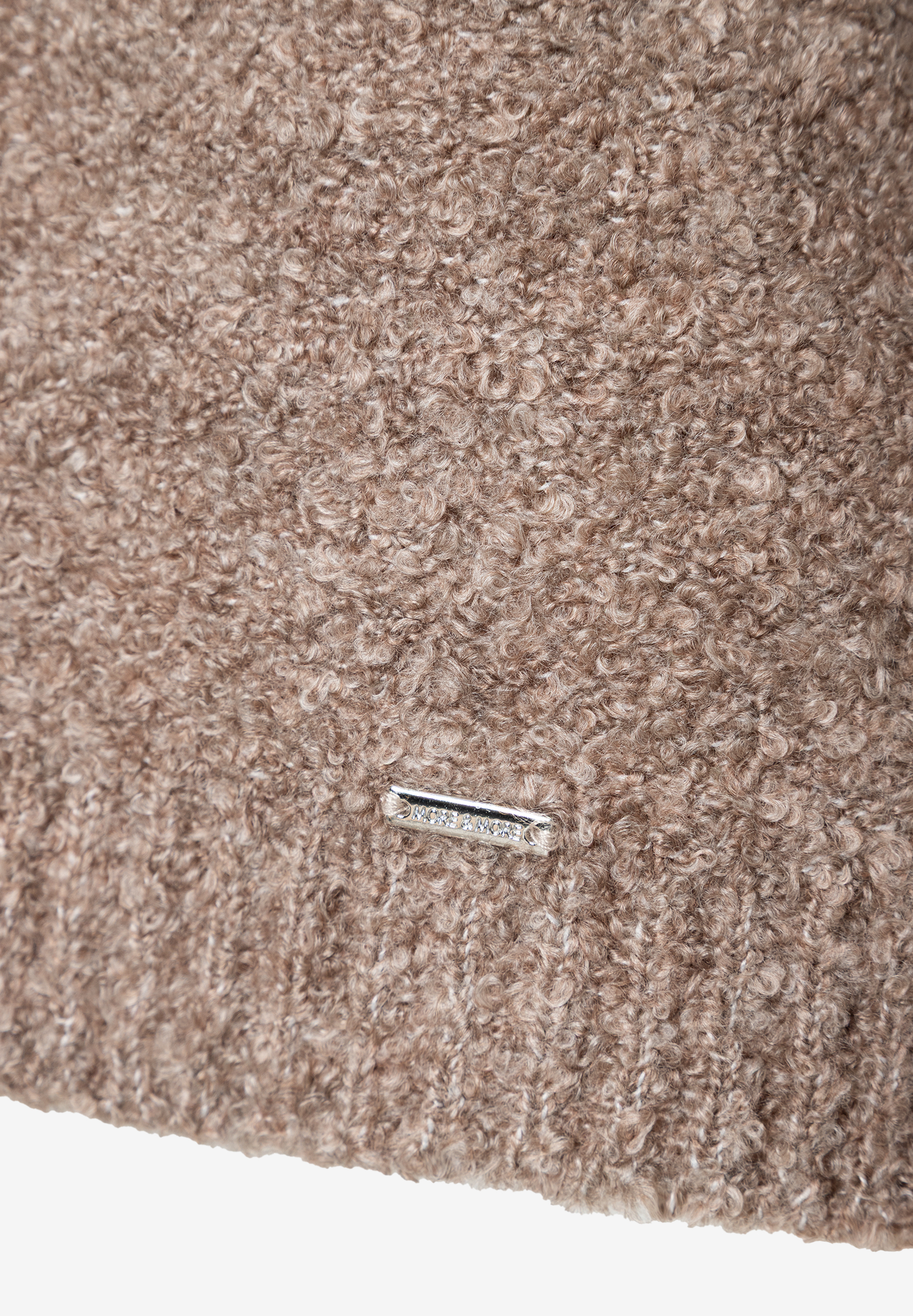 Nahaufnahme eines warmen, beigen Bouclé-Pullovers von MORE & MORE mit Logo-Metallplakette. Nahaufnahme eines warmen, beigen Bouclé-Pullovers von MORE & MORE mit Logo-Metallplakette.