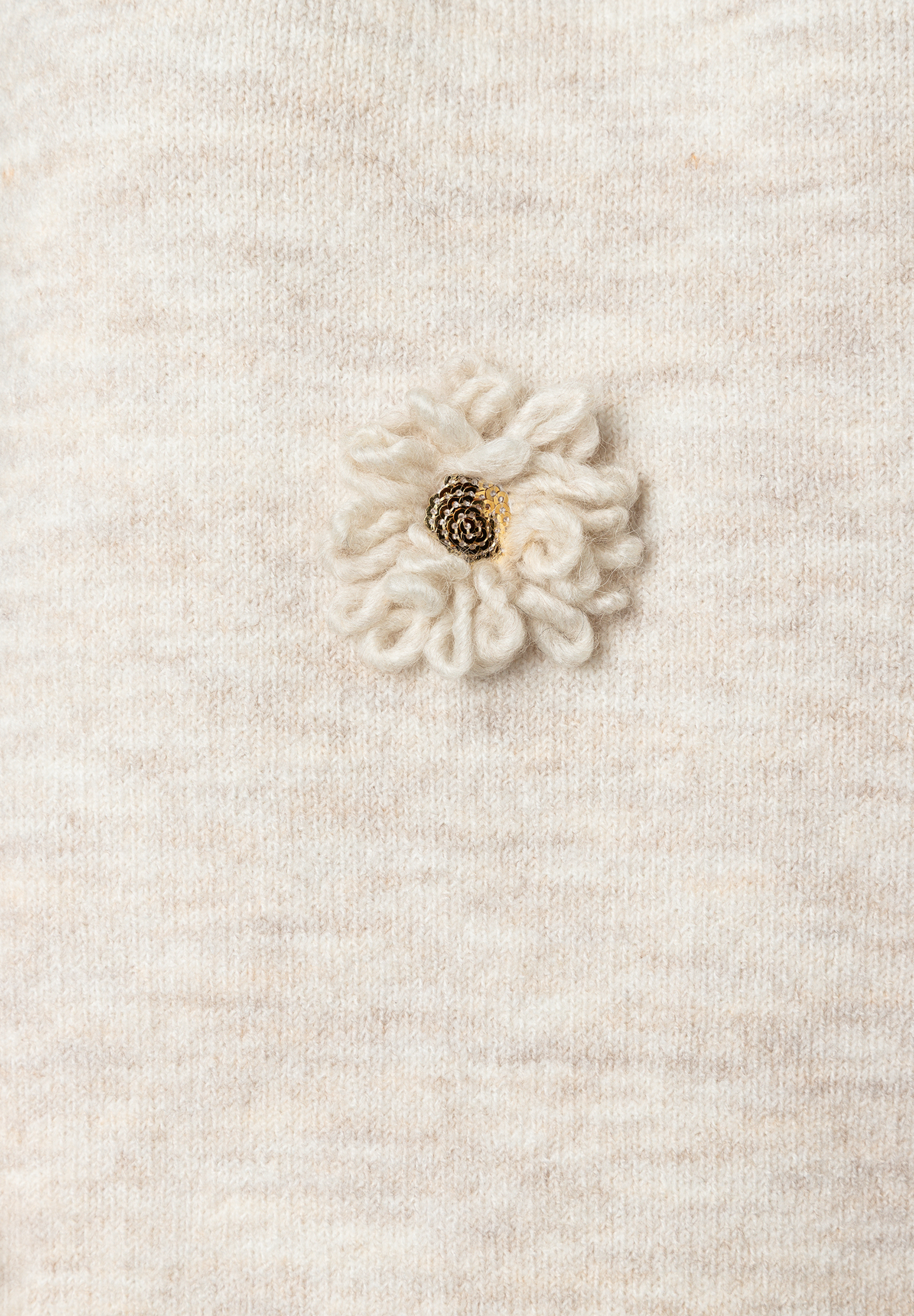 Detailaufnahme eines MORE & MORE-Oberteils, Strickware, mit applizierter Blume. Detailaufnahme eines MORE & MORE-Oberteils, Strickware, mit applizierter Blume.