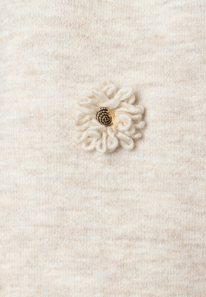 Detailaufnahme eines MORE & MORE-Oberteils, Strickware, mit applizierter Blume. Detailaufnahme eines MORE & MORE-Oberteils, Strickware, mit applizierter Blume.