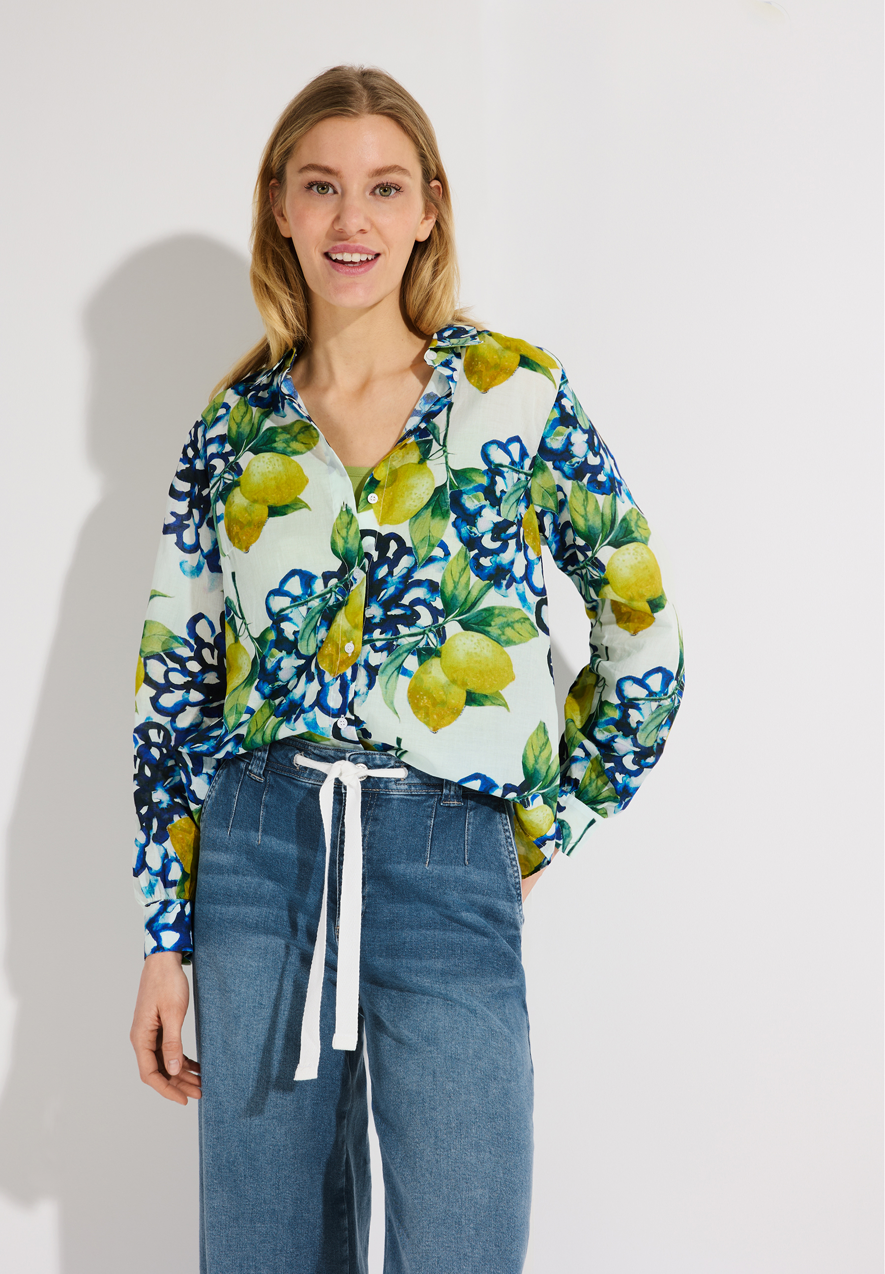 Eine Frau mit einer MORE & MORE Bluse mit Zitronen- und Blumenmuster.