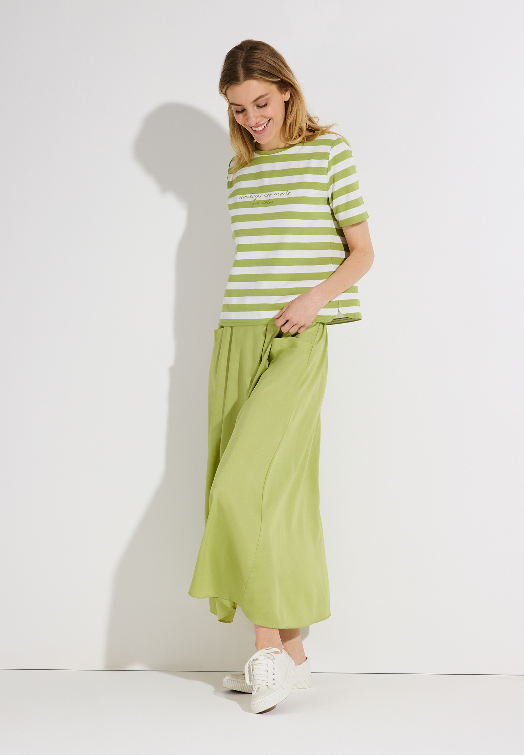 Eine Frau trägt ein MORE & MORE Jersey-Top mit grünen Streifen und passendem Rock.