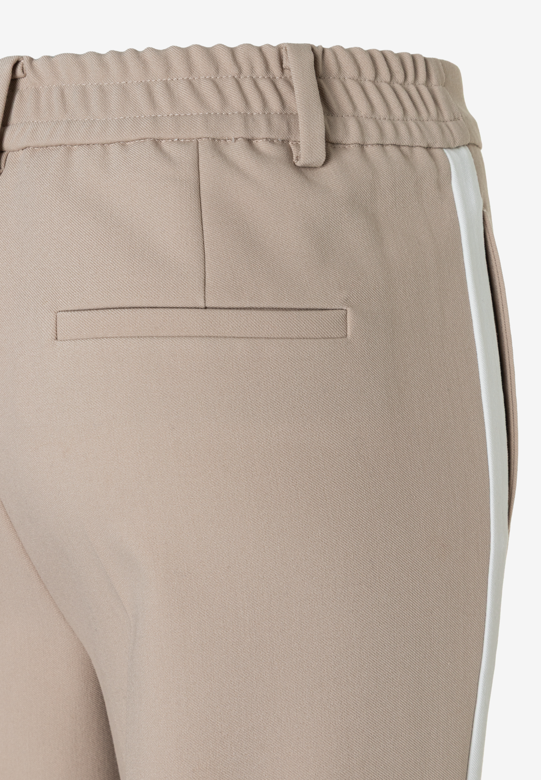 Detailaufnahme einer MORE & MORE Hose in Beige mit weißem Seitenstreifen und einer Gesäßtasche. Detailaufnahme einer MORE & MORE Hose in Beige mit weißem Seitenstreifen und einer Gesäßtasche.